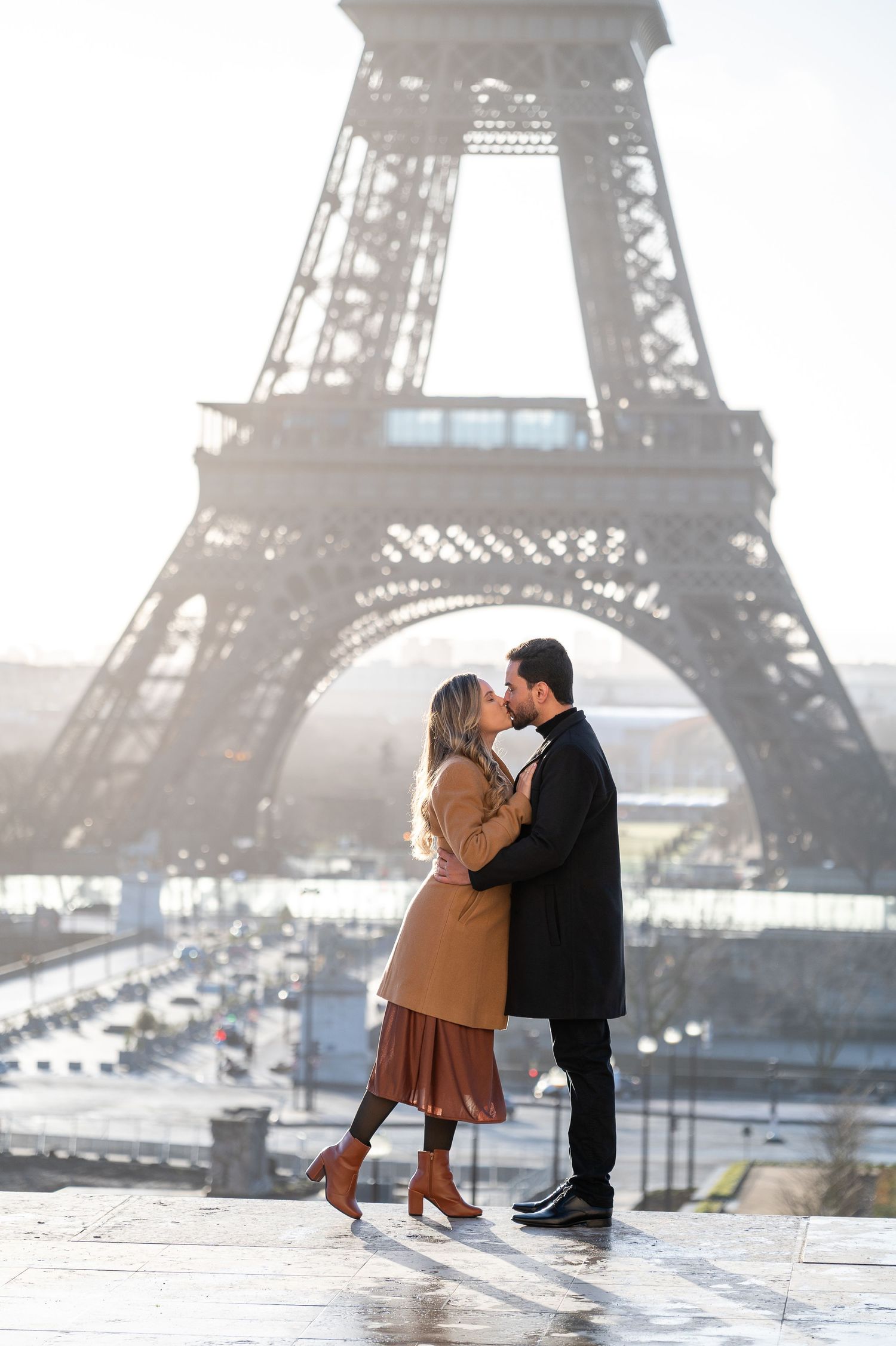 A romantic moment captured beneath the iconic Eiffel Tower on a misty Parisian morning.