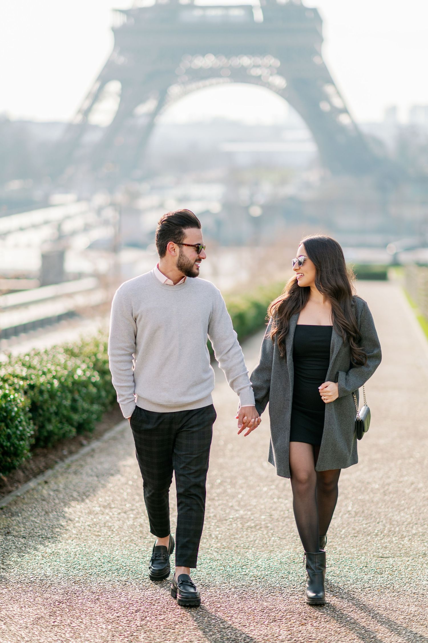 A couple walks hand in hand on a path near the Eiffel Tower in Paris during a romantic misty morning.