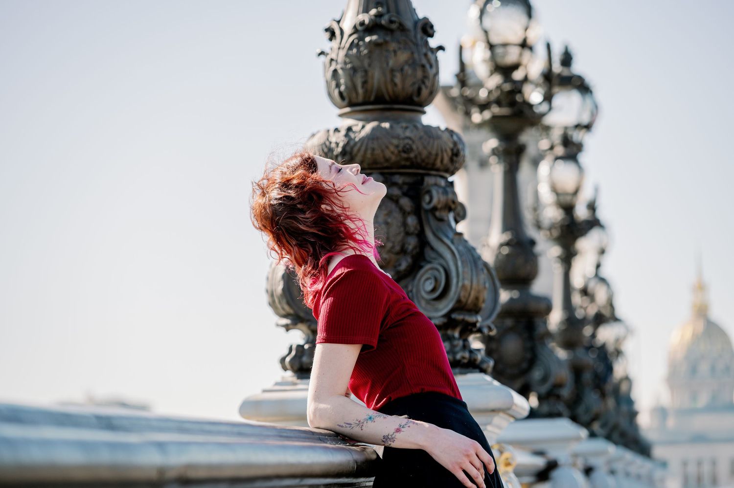 A woman in red attire dances gracefully at sunset against a backdrop of ornate street lamps and city architecture.