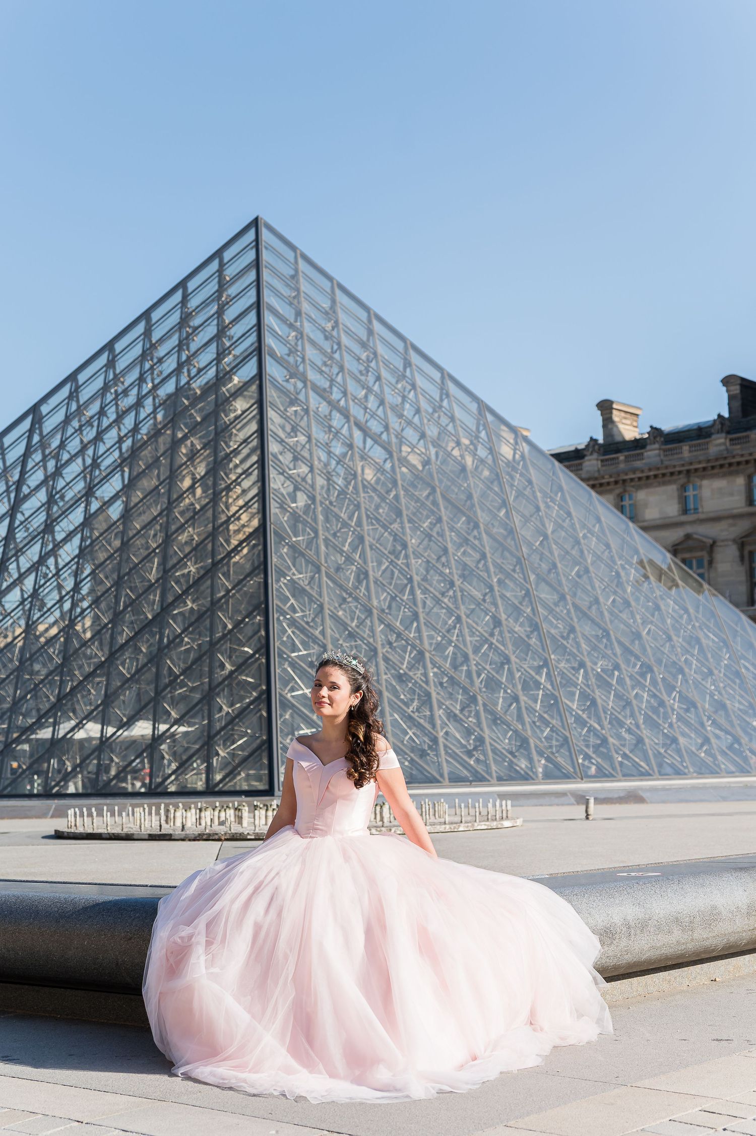 Bride in pink tulle ball gown posing in front of Louvre glass pyramid in Paris, France.