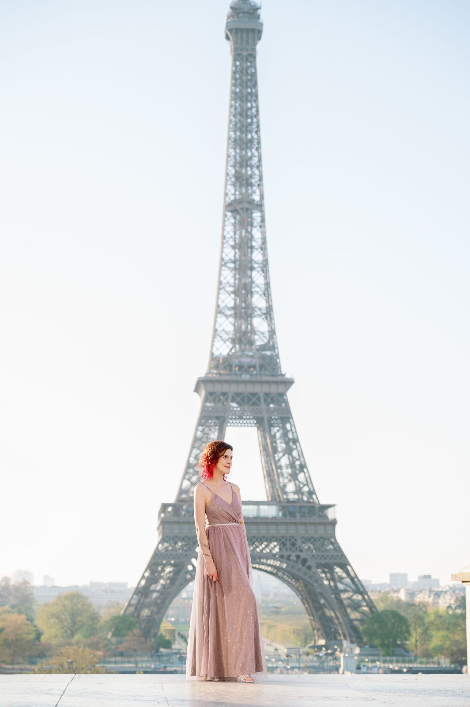 Four frames showing a pink-dressed figure posing in front of the Eiffel Tower in Paris on a misty morning.