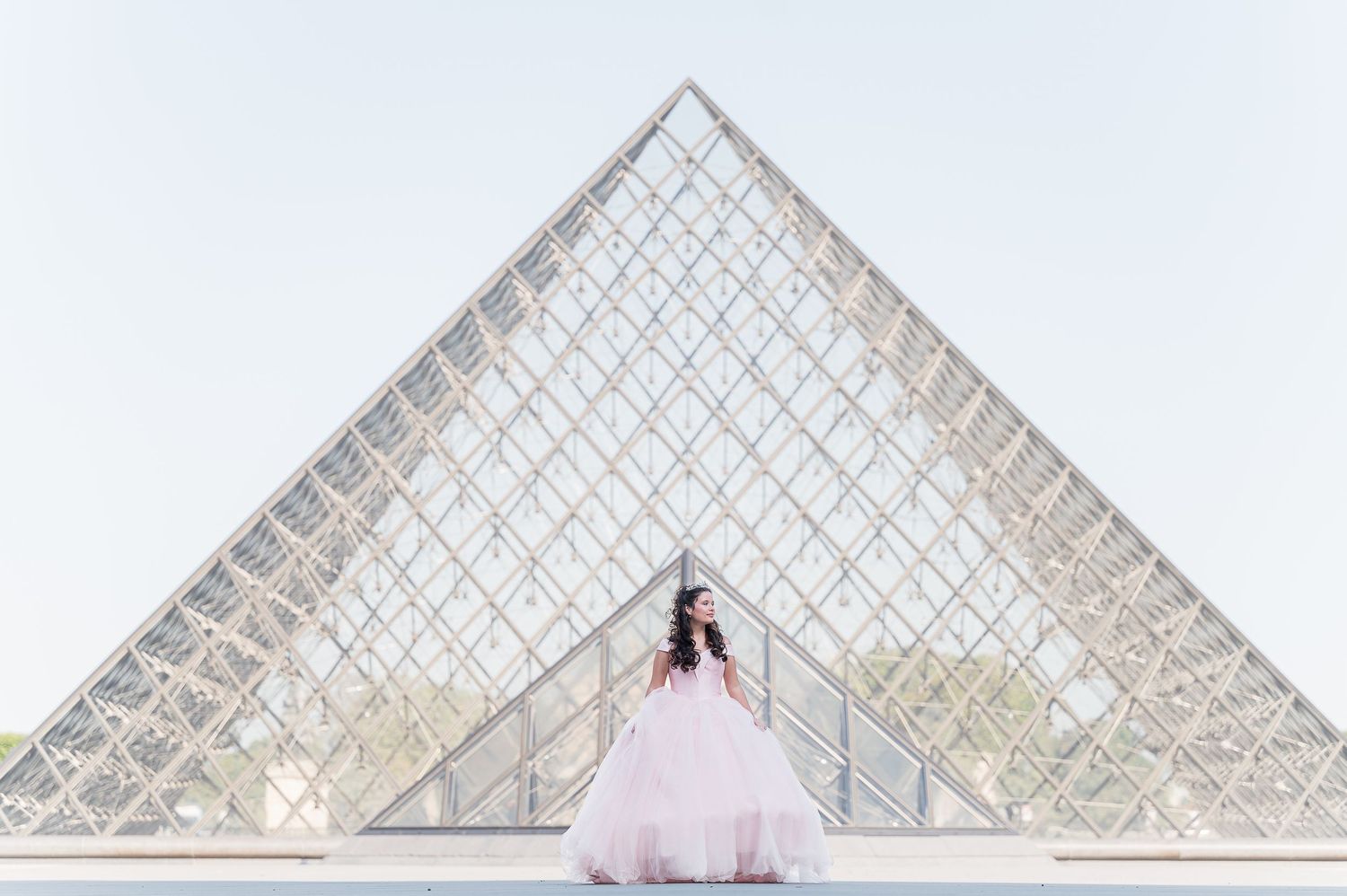 Woman in pink ball gown poses before the Louvre Pyramid in Paris, France.