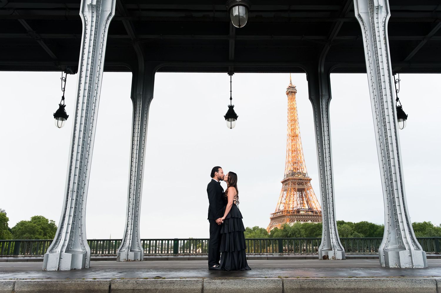 Couple embracing on Bir-Hakeim Bridge in Paris with the iconic Eiffel Tower glowing in the background at dusk.