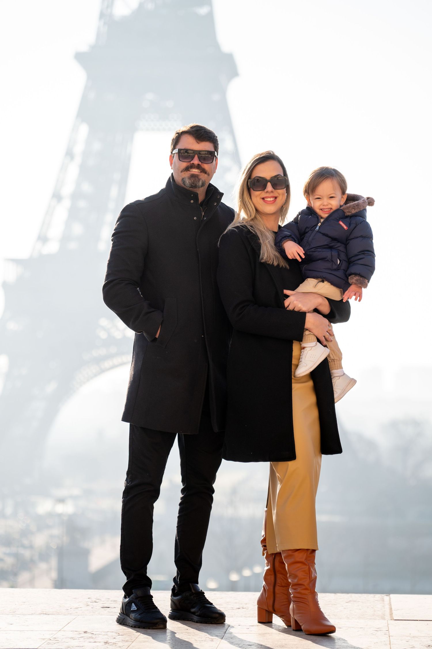 Stylish family in winter outfits posing with Eiffel Tower in background on foggy day.