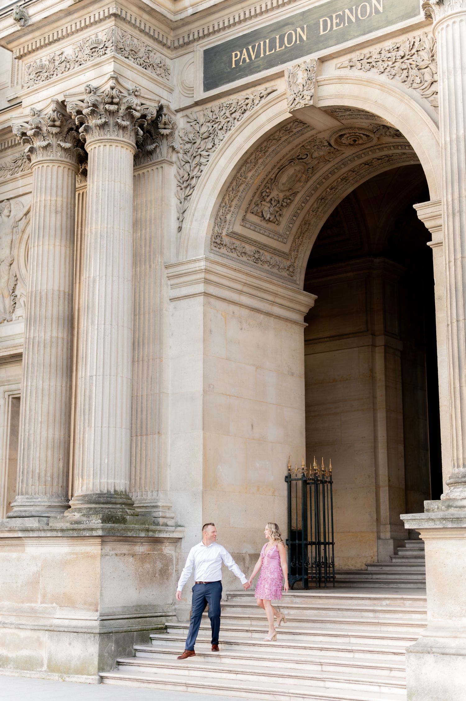 A couple poses on the grand steps of the Pavillon Denon at the Louvre Museum.