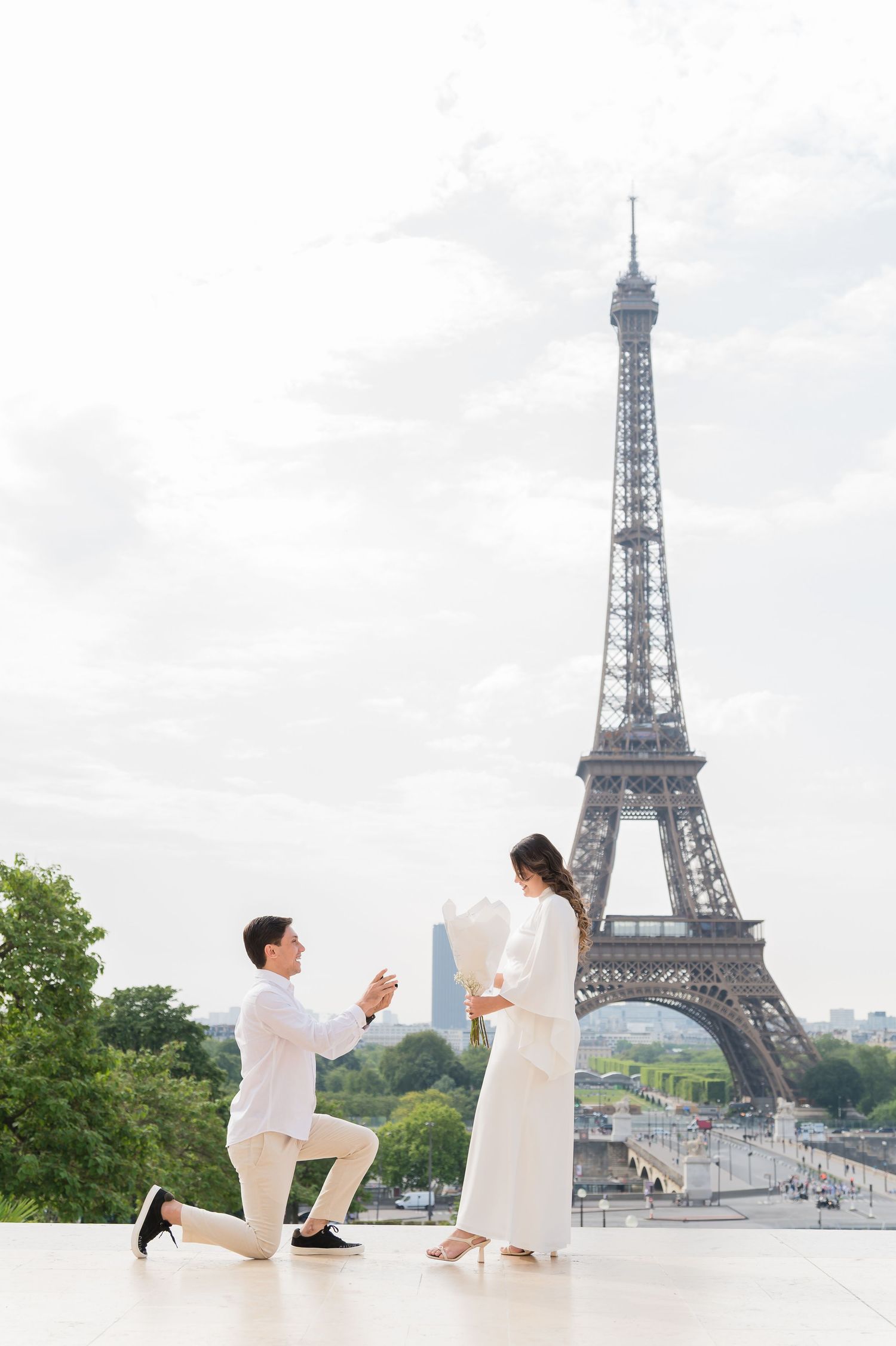 A romantic marriage proposal scene in front of the iconic Eiffel Tower in Paris on a cloudy day.