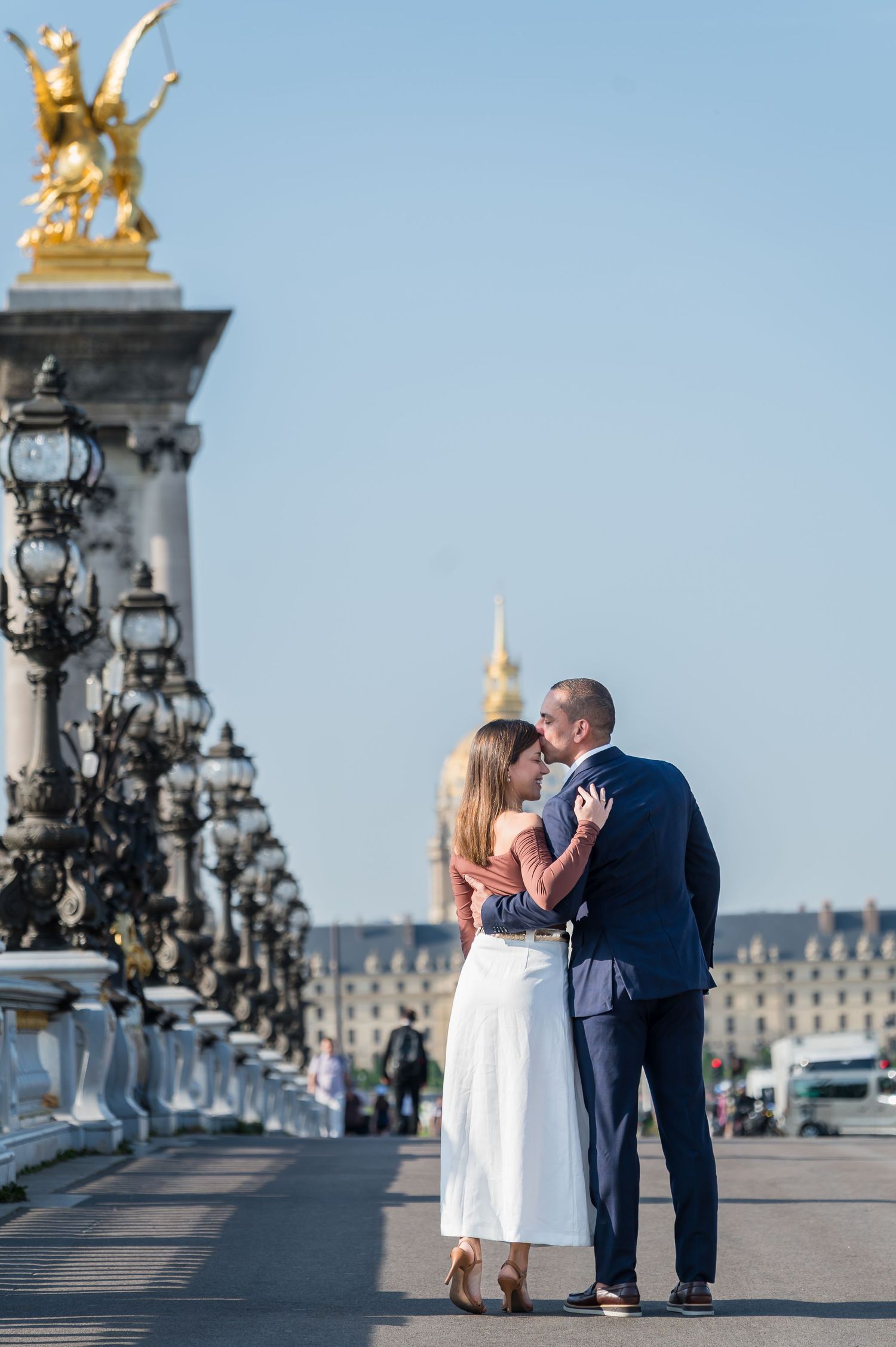 A couple embraces on the iconic Pont Alexandre III bridge in Paris with its ornate golden statues and lampposts.