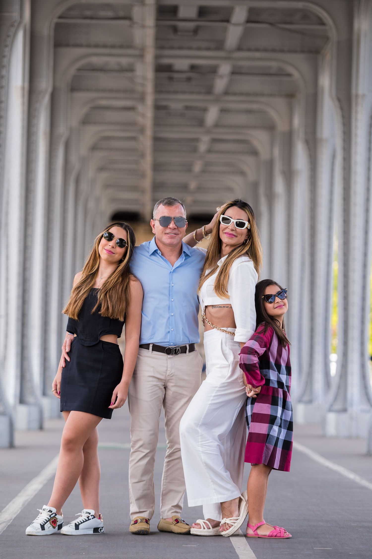 A group of people in sunglasses pose together beneath an elegant colonnade structure with repeating archways.