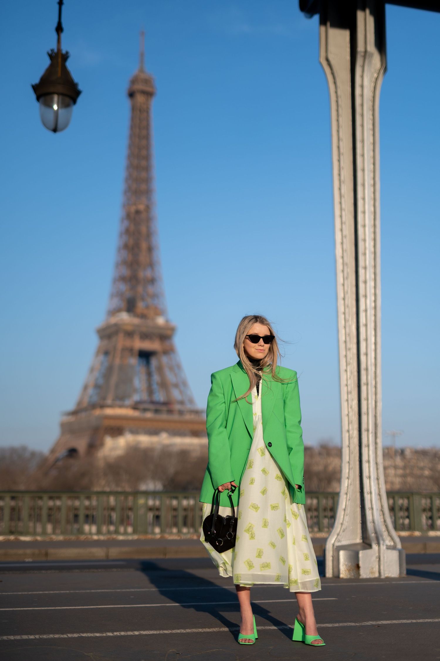 A bright green blazer and dress outfit stands out against the iconic Eiffel Tower backdrop in Paris on a sunny day.