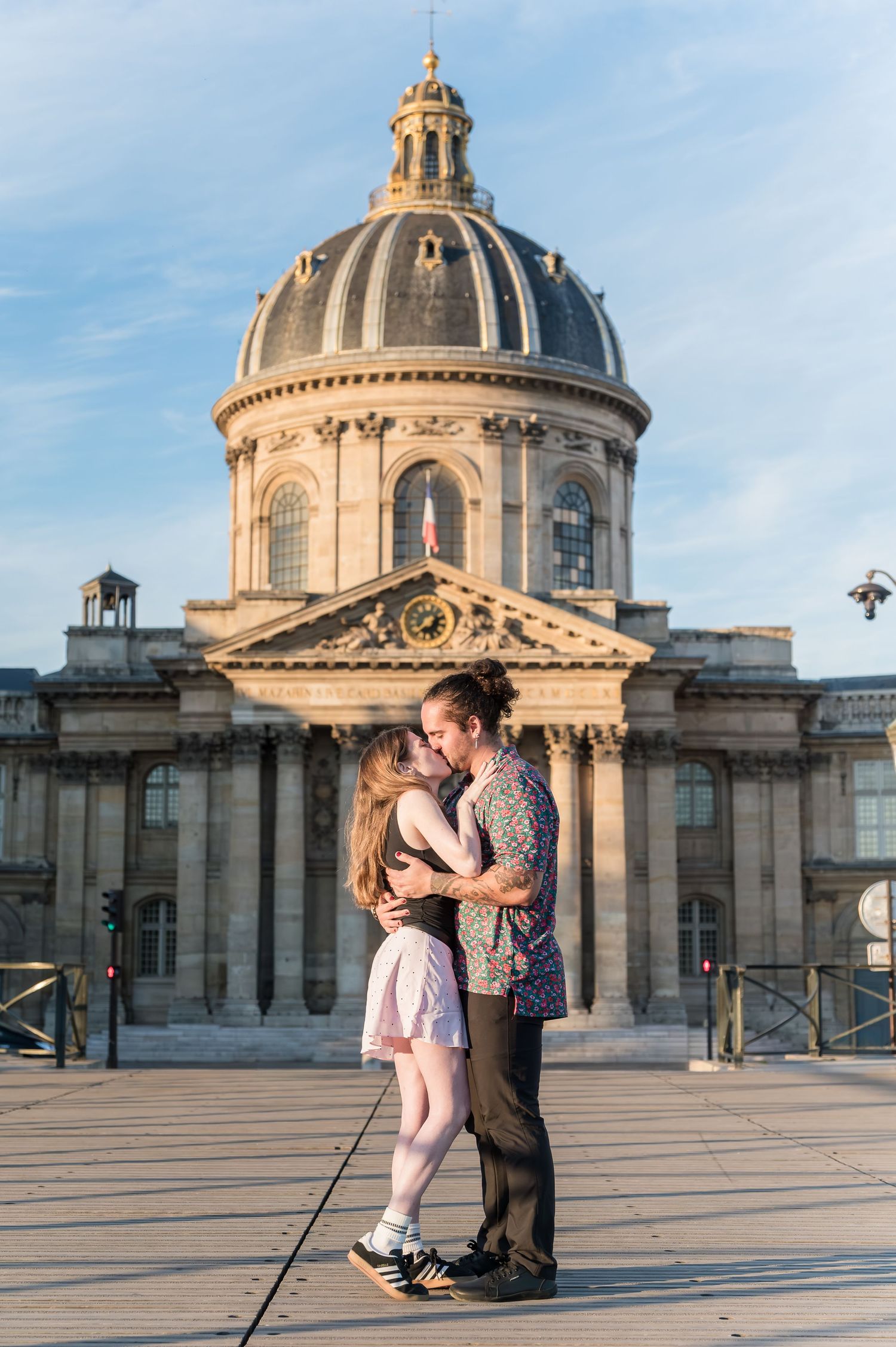 Couple sharing a romantic kiss on a bridge in Paris with the Institut de France dome in the background.