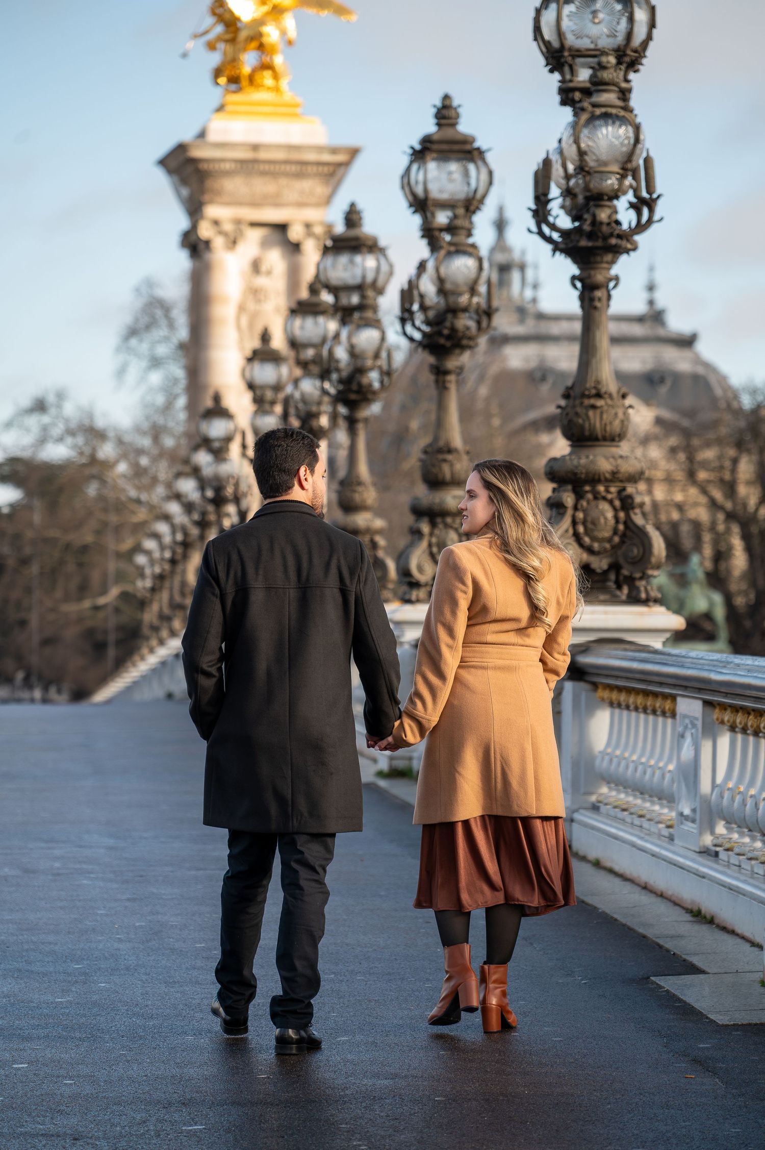 A couple strolls hand in hand along the ornate Pont Alexandre III bridge in Paris.