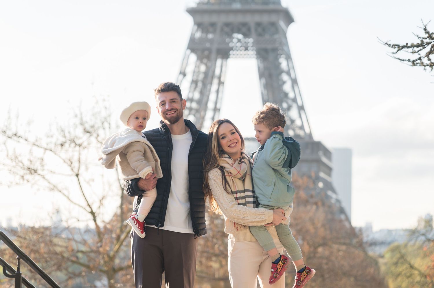 Happy family of four posing in front of the Eiffel Tower in Paris on a sunny day.