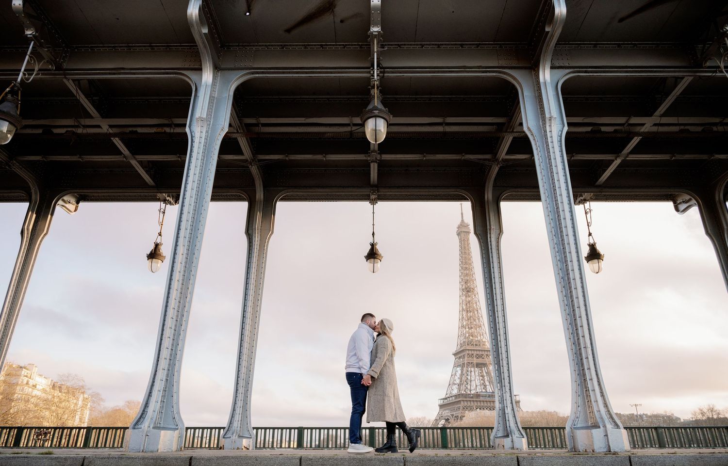 Couple sharing a romantic moment under Bir-Hakeim Bridge with the Eiffel Tower in the background at sunset in Paris.