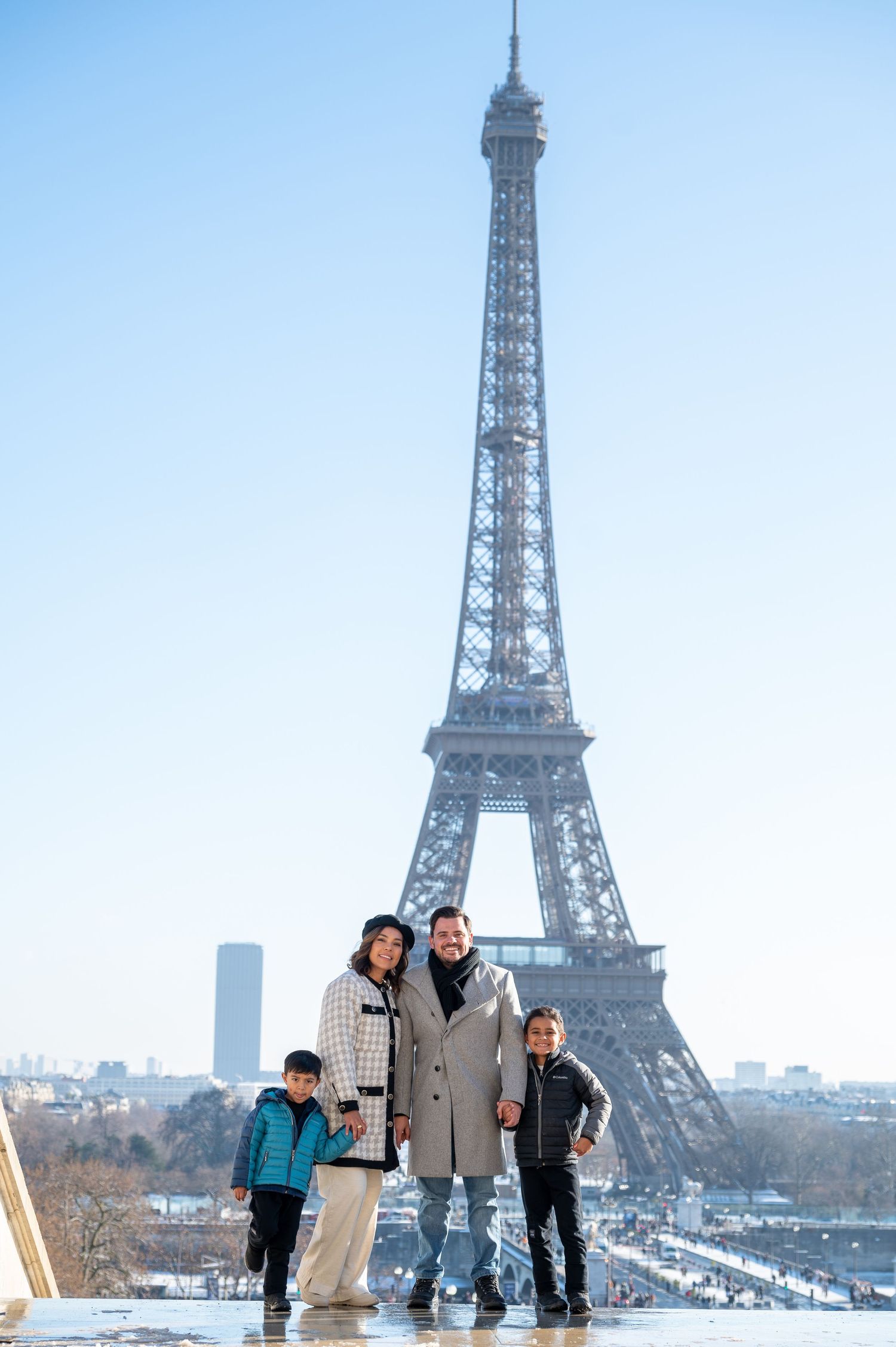 Tourists pose for photos with the iconic Eiffel Tower in Paris during winter with snow on the ground.