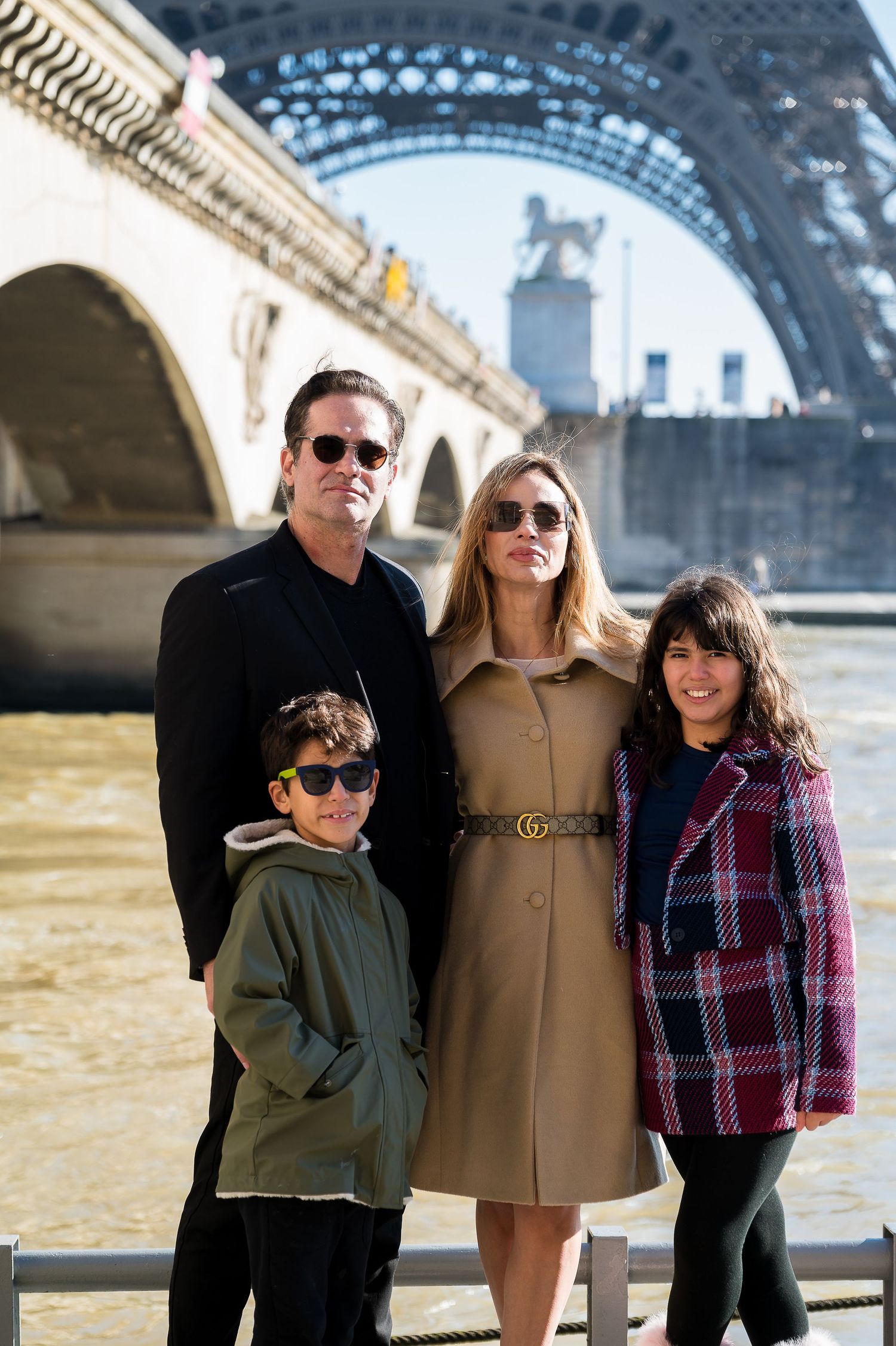 A family group poses beneath the Eiffel Tower's iron arches on a bright day in Paris.
