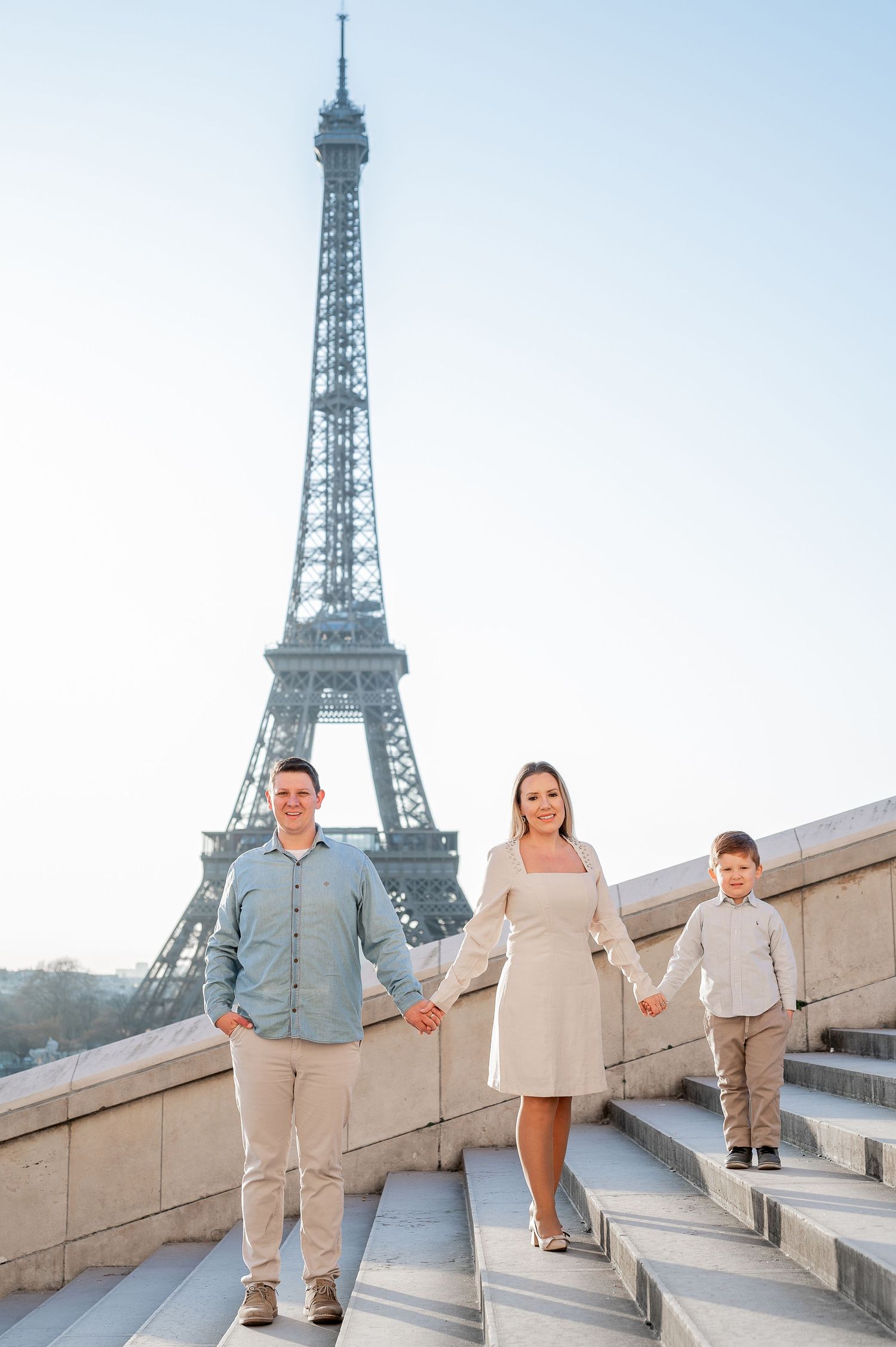 Family holding hands while walking up Trocadero steps with Eiffel Tower view.
