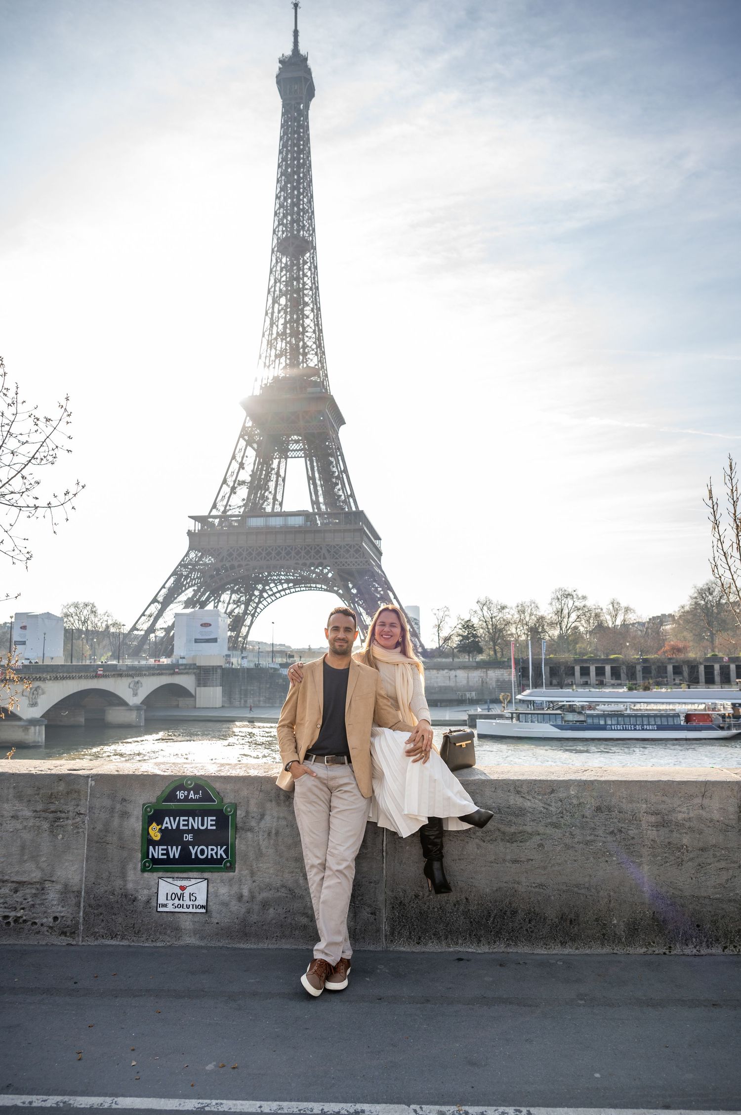 A couple stands along the Seine River with the majestic Eiffel Tower rising behind them.