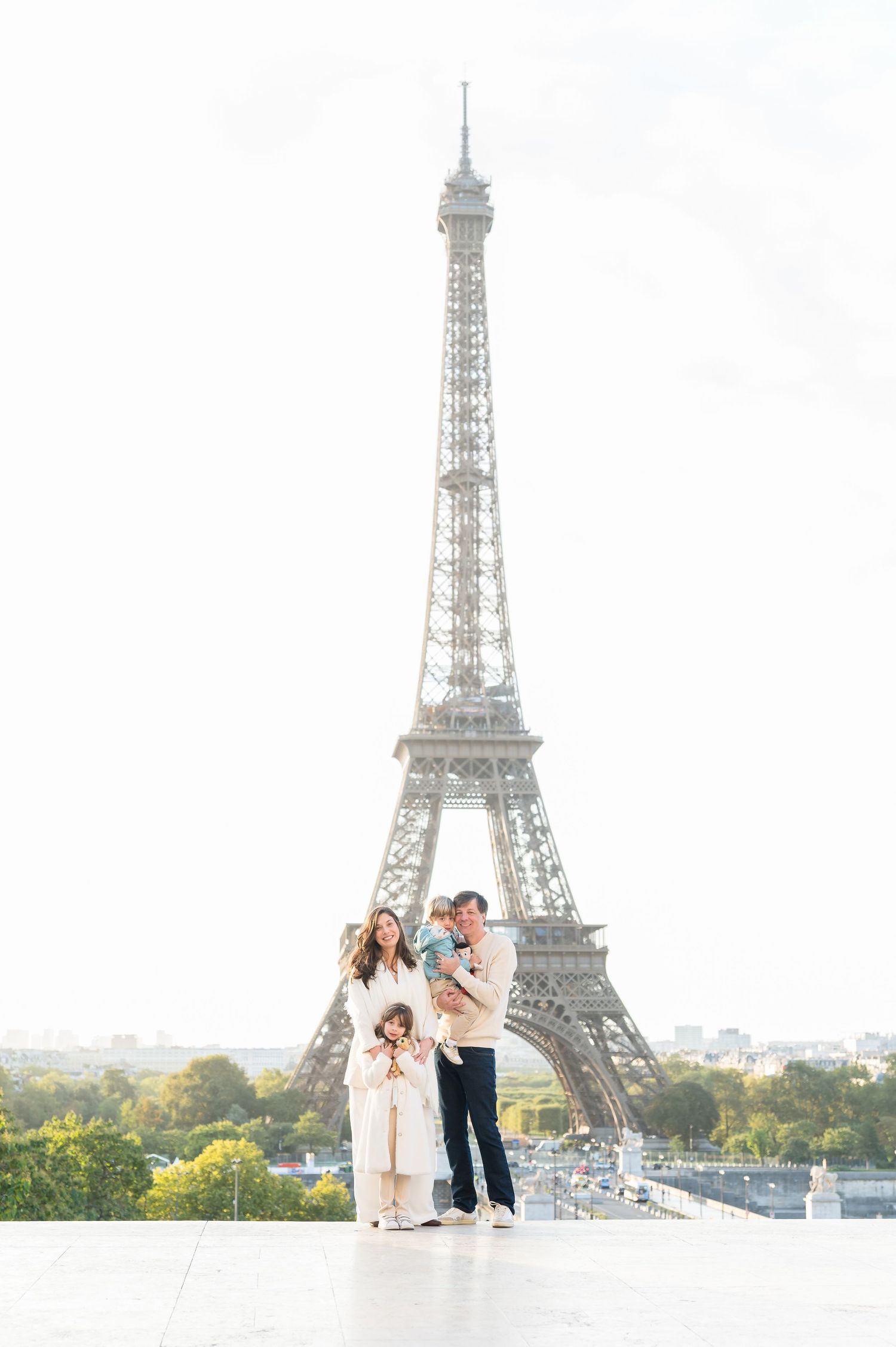 A family stands together on a terrace overlooking the iconic Eiffel Tower in Paris on a bright autumn day.