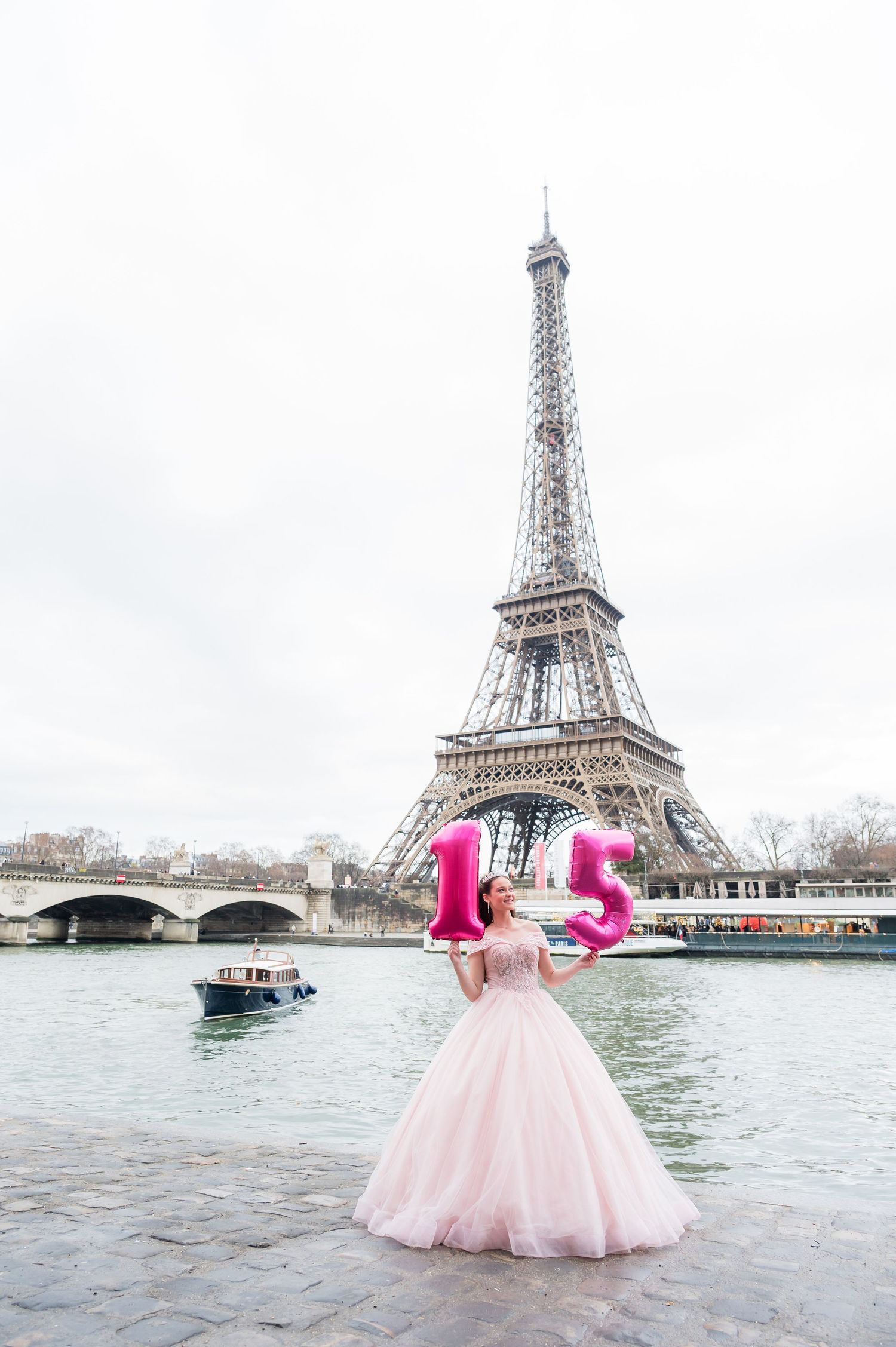 A pink ballgown dress photographed from different angles near the Eiffel Tower in Paris with boats on the Seine River.
