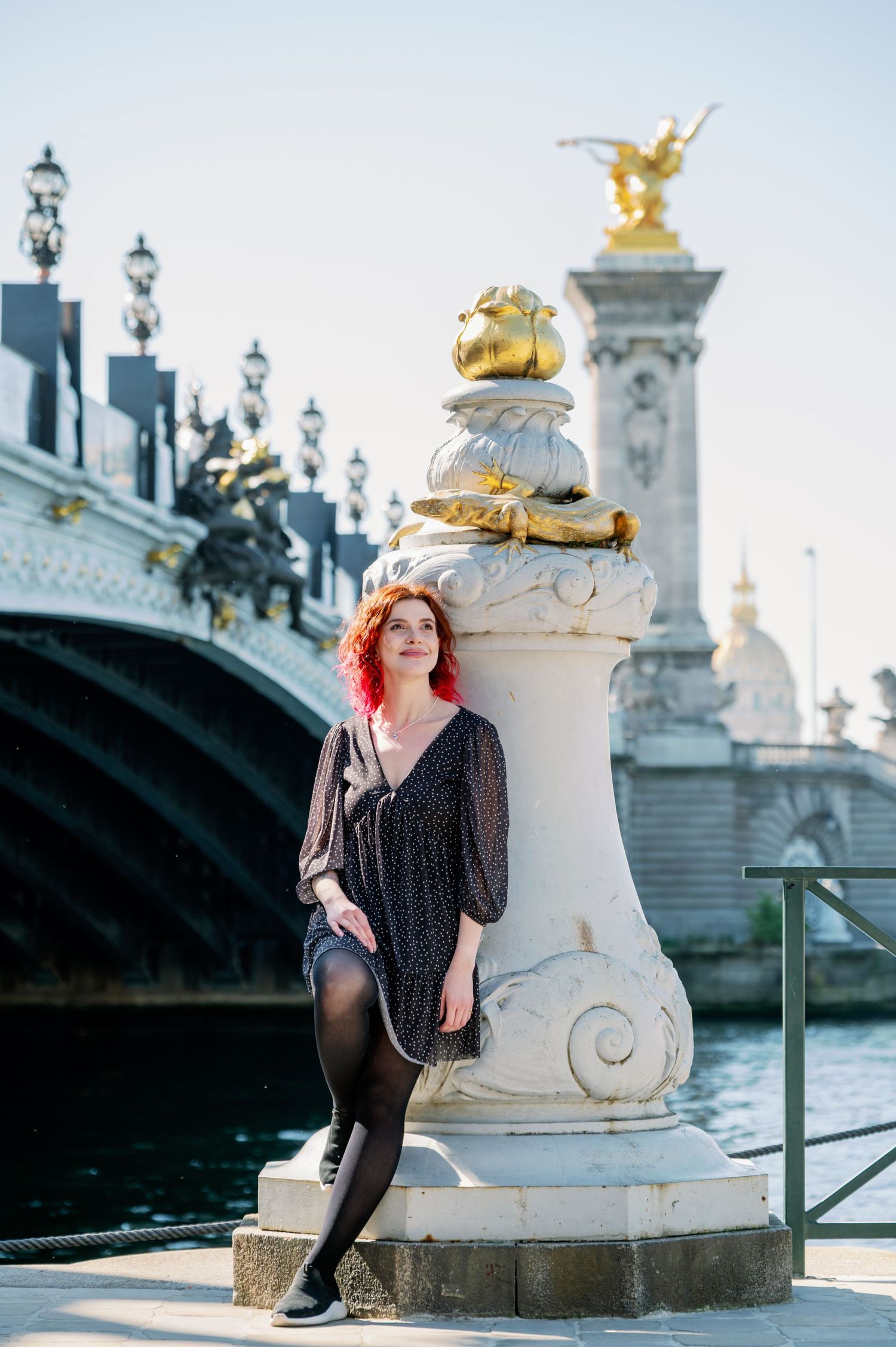 An ornate white stone bridge pillar with gold accents stands along the Seine River in Paris.
