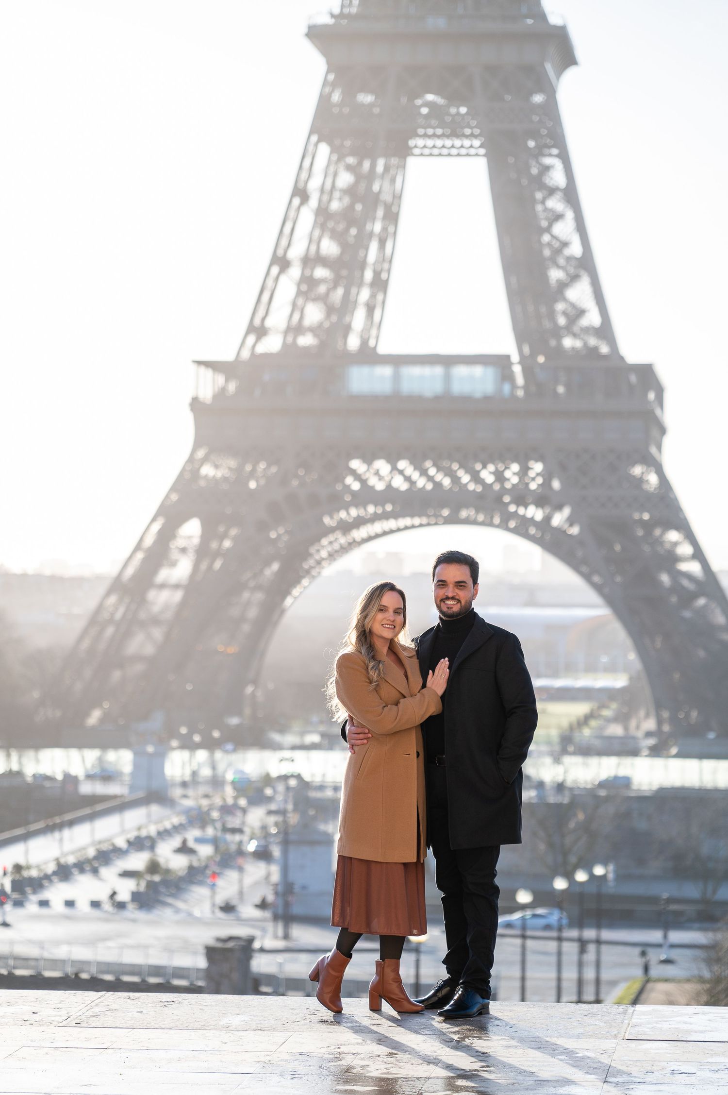 A stylish couple poses for a portrait in front of the Eiffel Tower on a bright winter day.