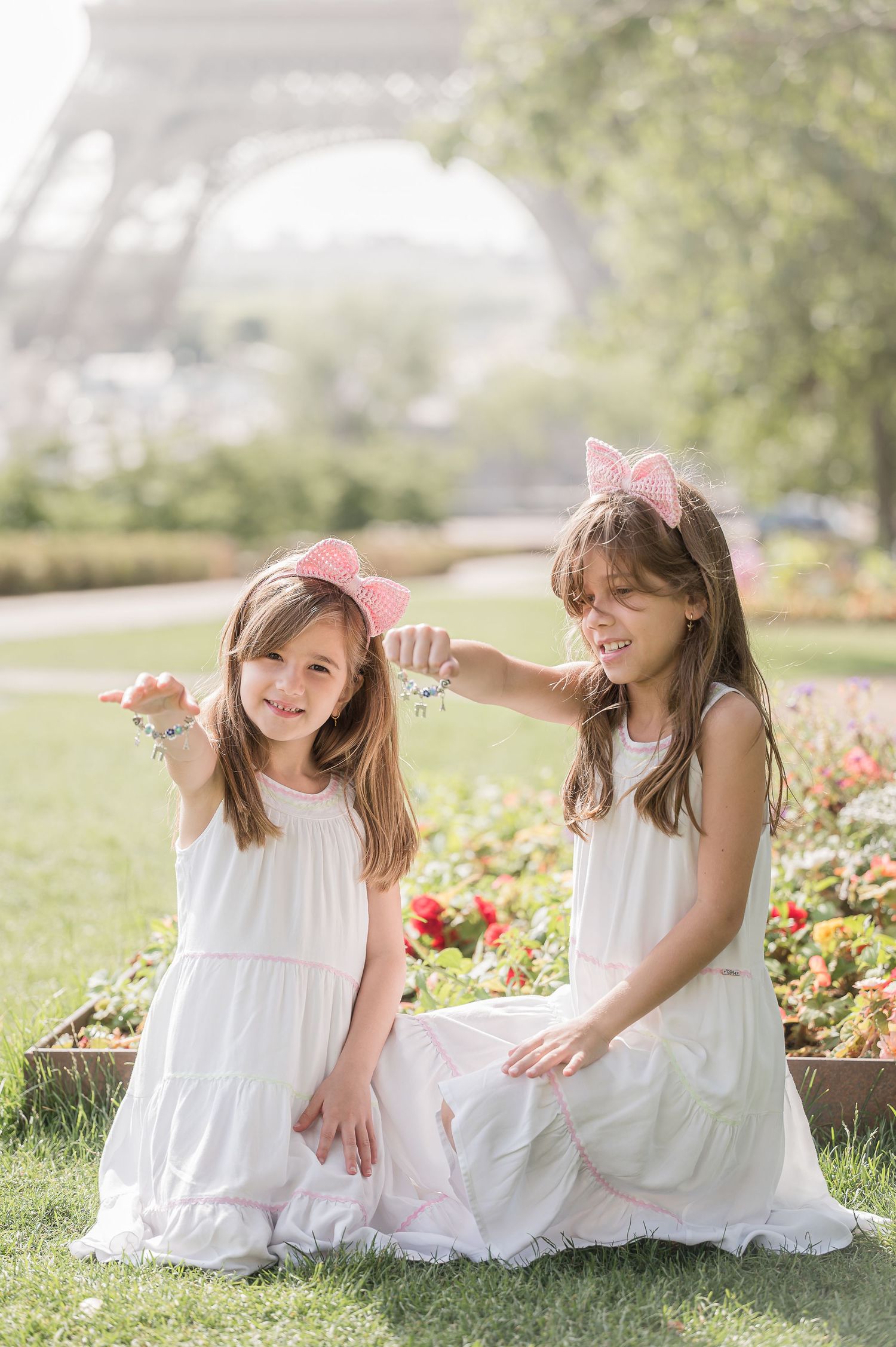 Two girls in white dresses with pink cat ear headbands pose near the Eiffel Tower in Paris.