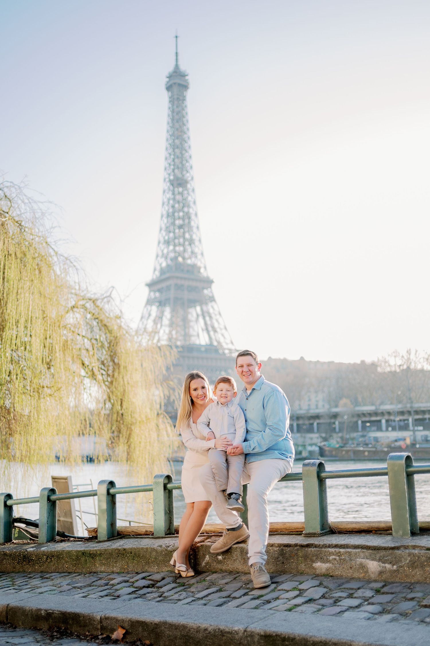 Family portrait by the Seine River with Eiffel Tower and willow trees in background.