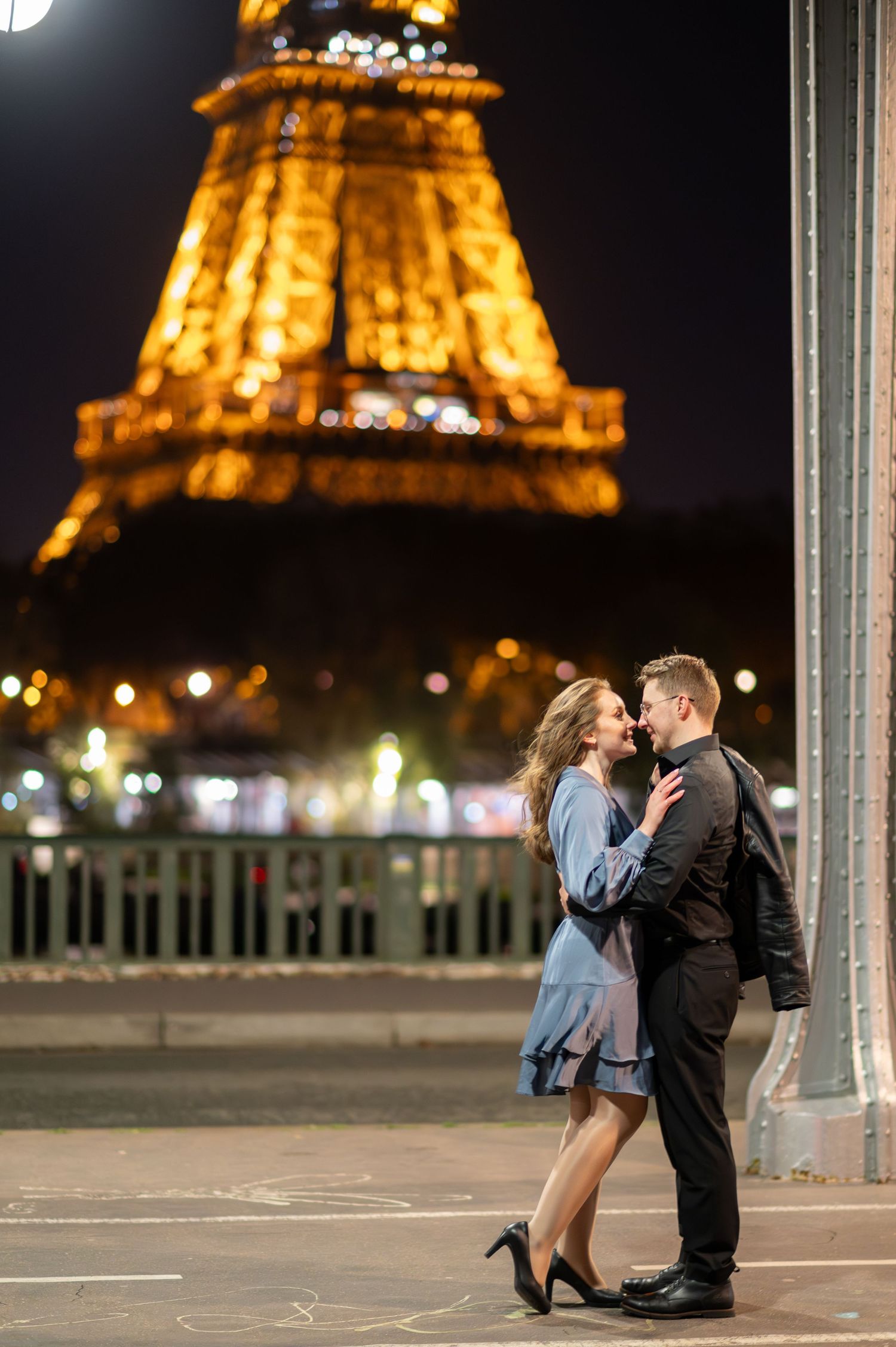 A romantic couple embraces at night with the illuminated Eiffel Tower glowing warmly in the background in Paris.