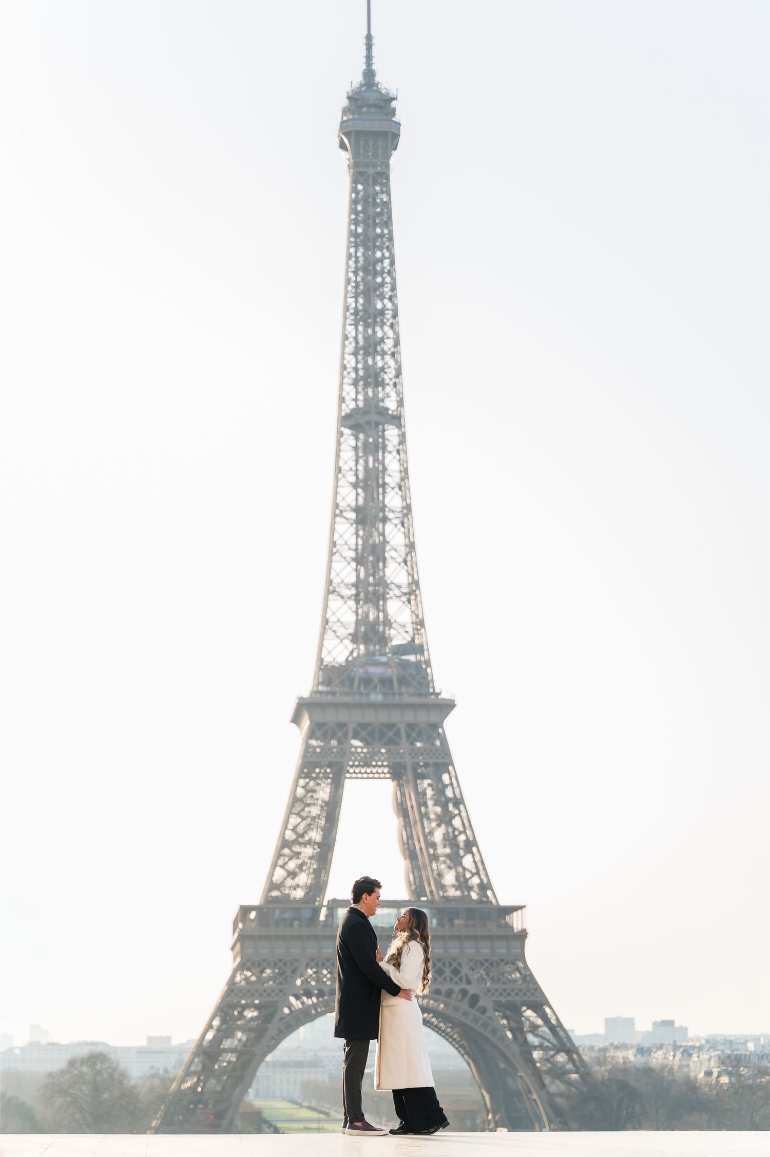 Romantic couple embracing in front of the Eiffel Tower in Paris, France on a bright sunny day.