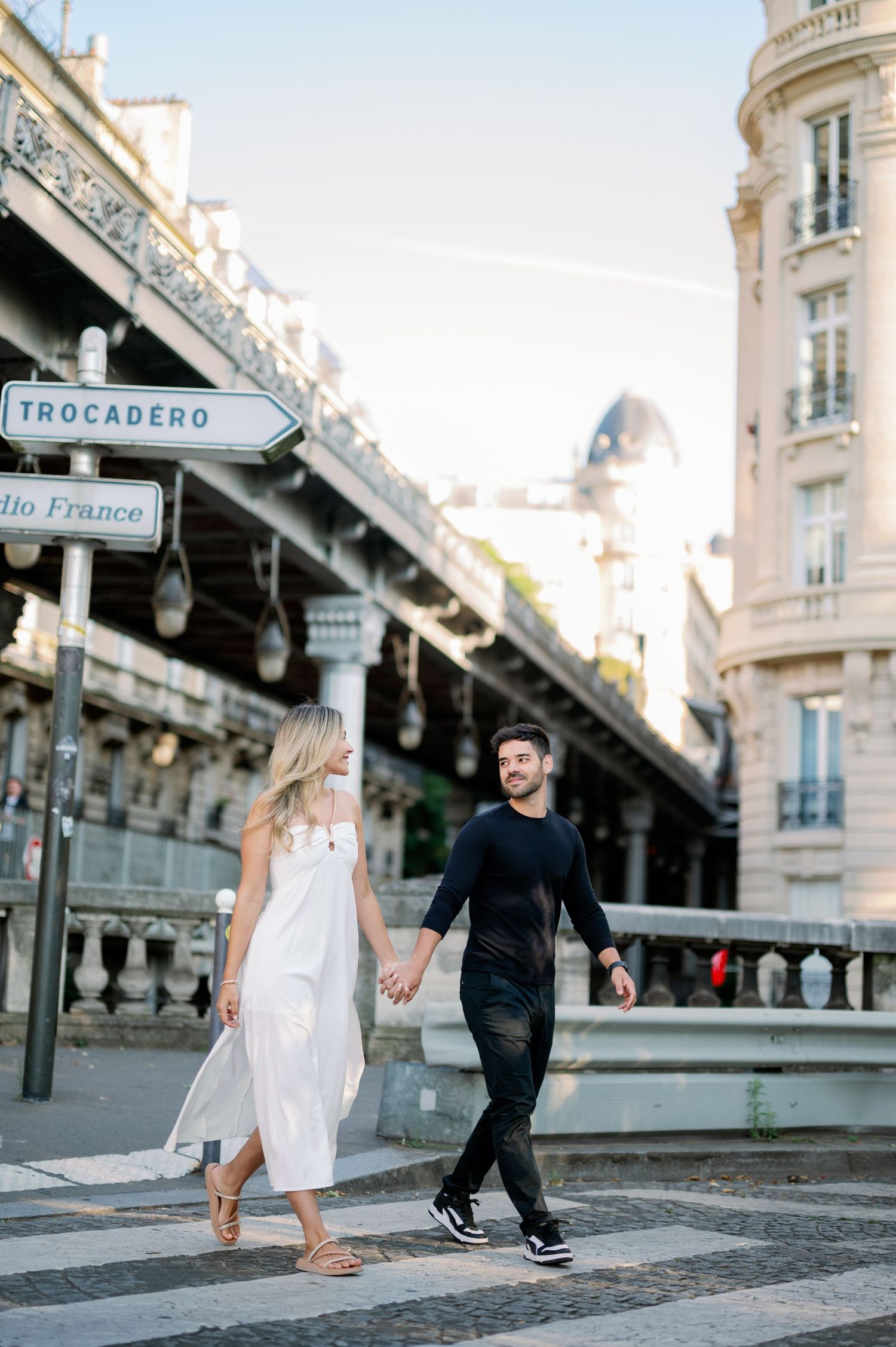 A couple strolls hand in hand past the Trocadero street sign in Paris.