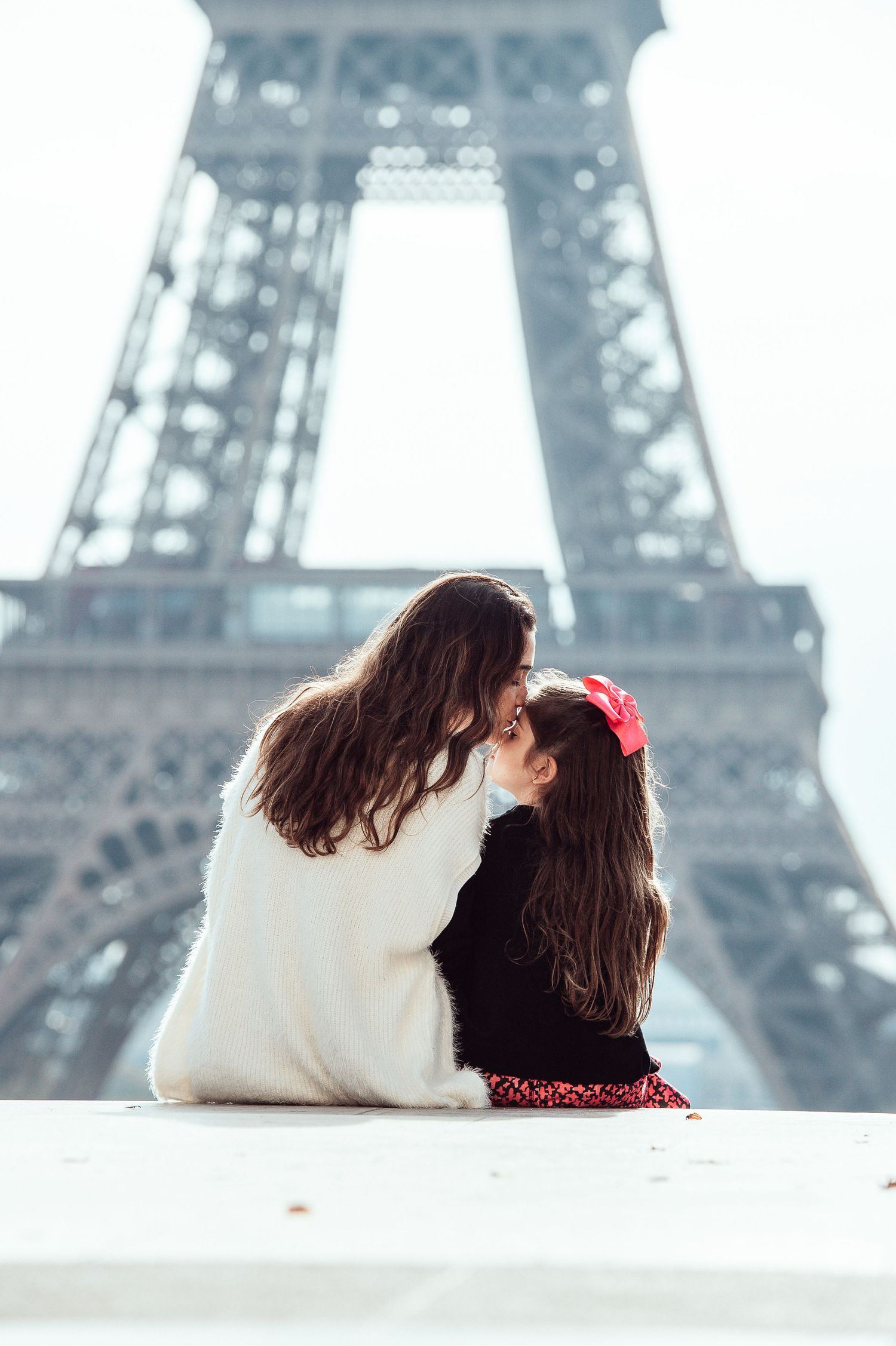 Two people in warm clothes share a tender moment while sitting in front of the iconic Eiffel Tower in Paris.