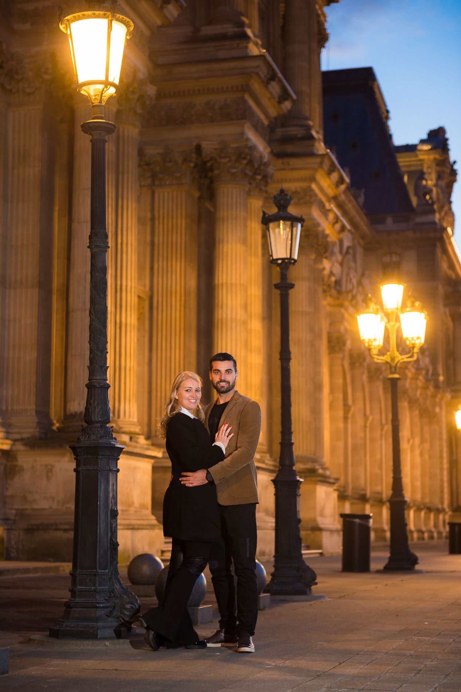 Two people dance together under warm glowing lanterns along a columned walkway at dusk.