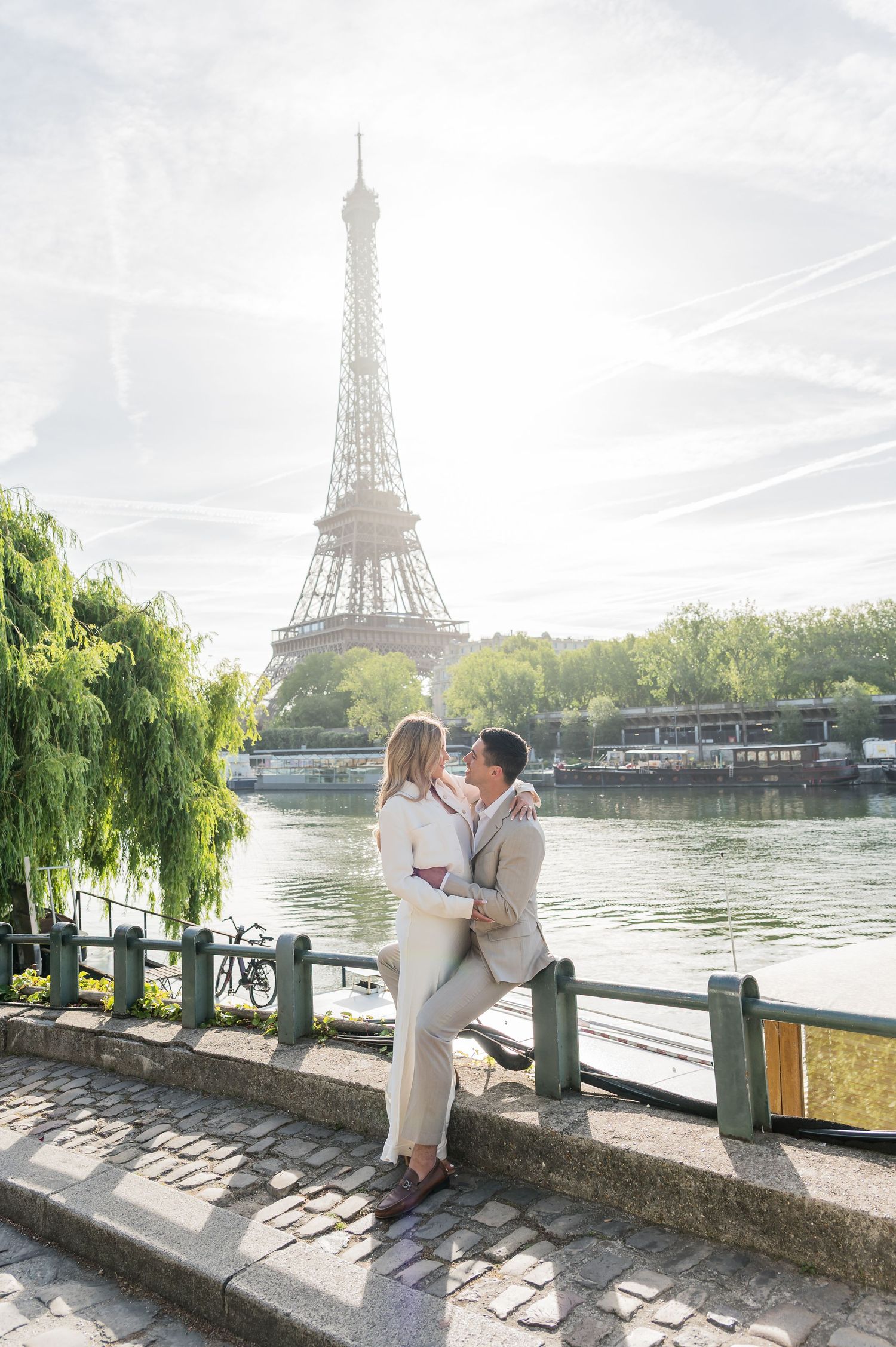 Romantic moment along the Seine River in Paris with the iconic Eiffel Tower visible in the background on a misty morning.