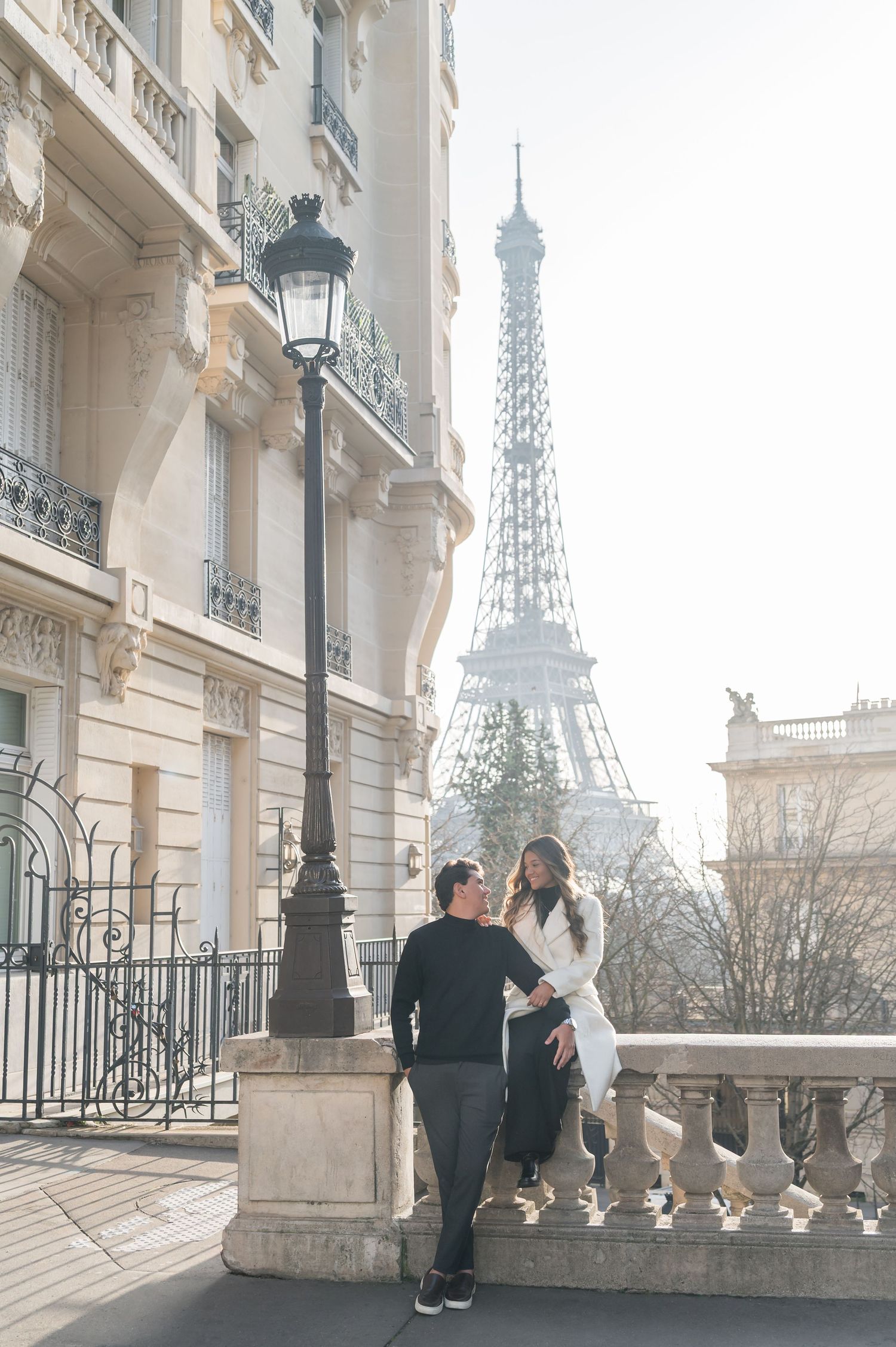 Couple sharing a romantic moment near the Eiffel Tower in Paris, France, with classic Haussmann architecture nearby.