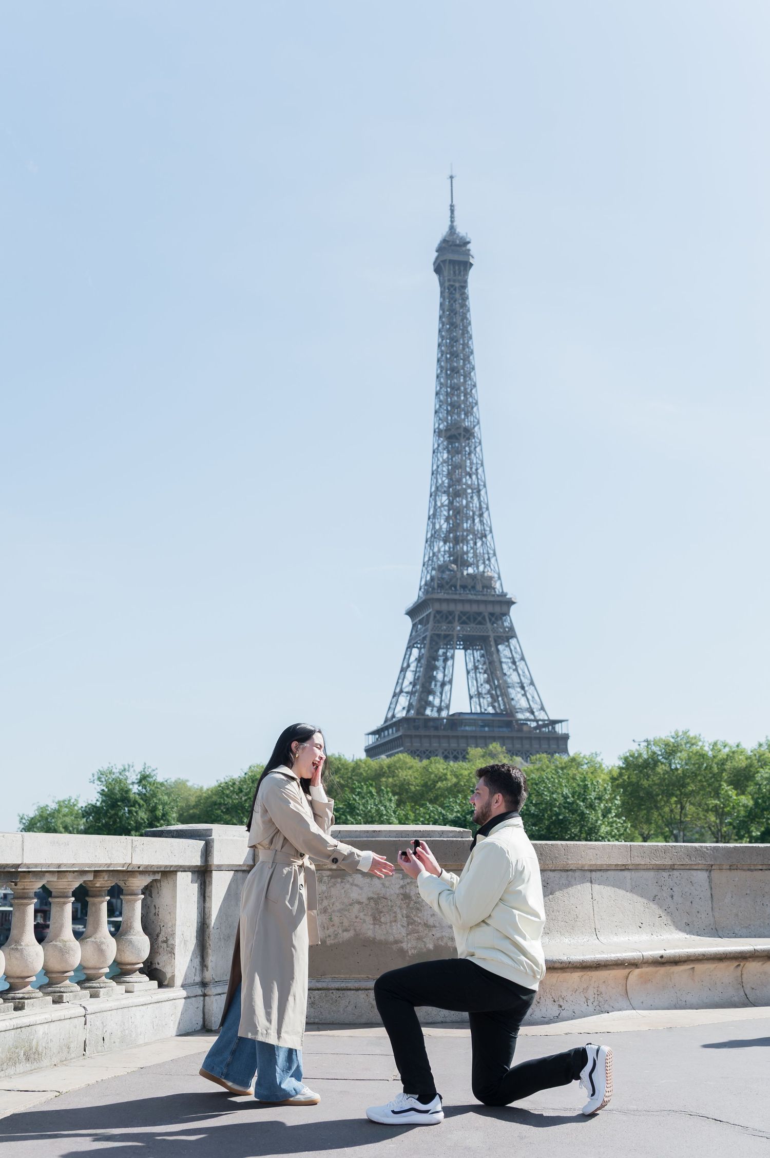 Man proposes to woman on one knee near Eiffel Tower in Paris on a sunny day.