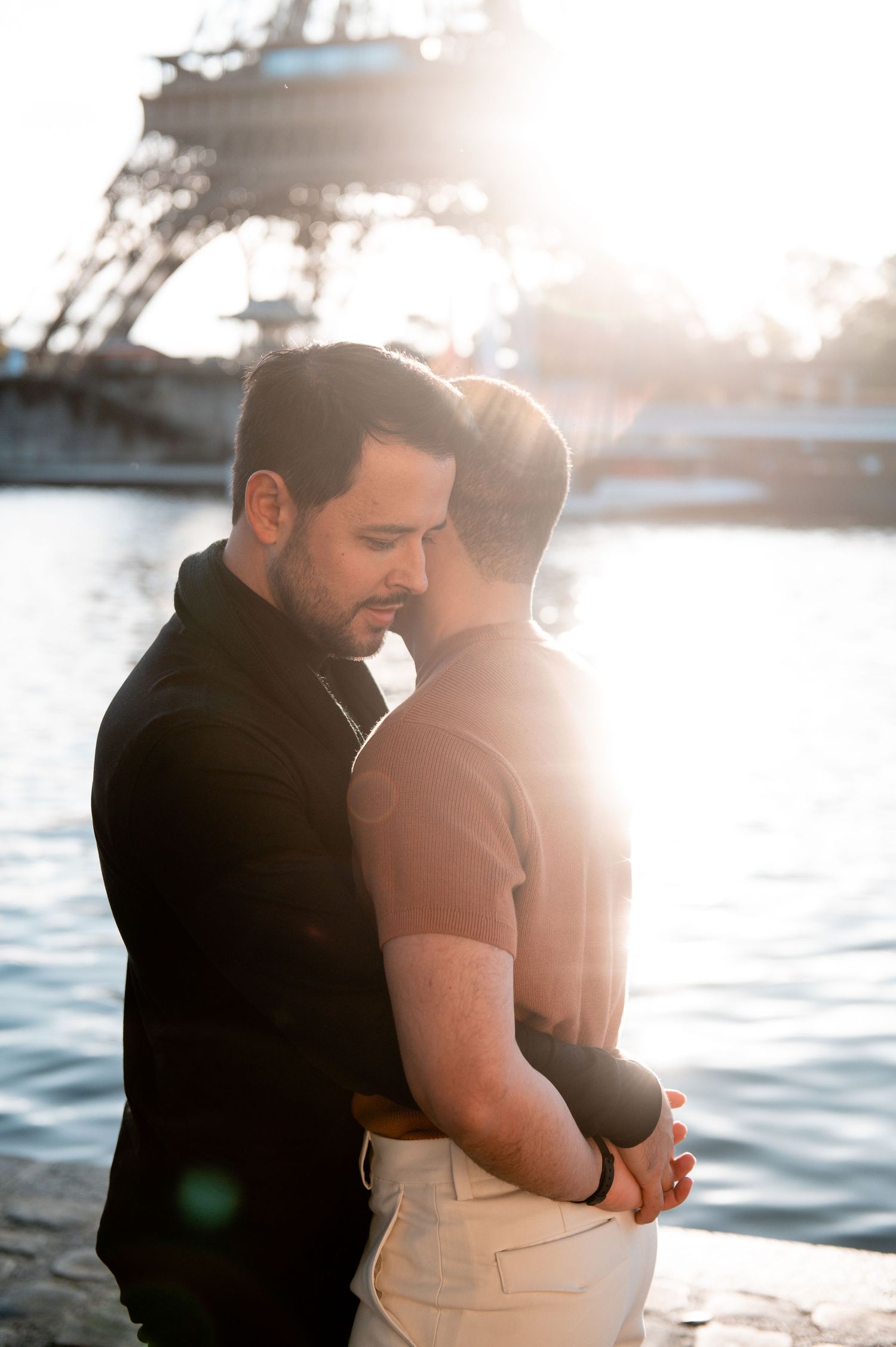 A romantic couple embraces by the water during golden hour with sunlit reflections creating a dreamy atmosphere.
