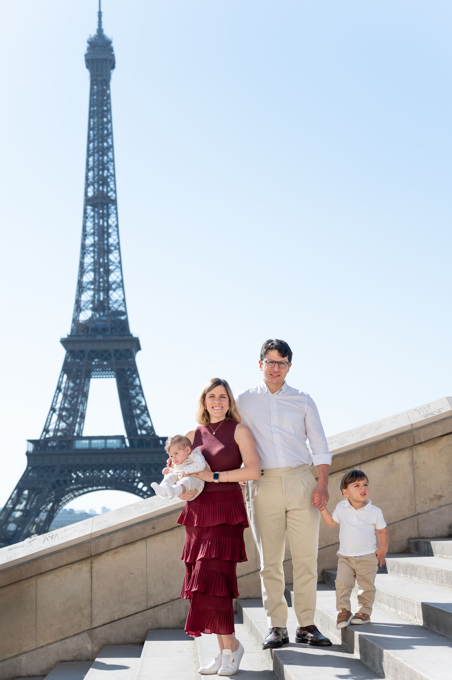 Family stands together on stone steps with the iconic Eiffel Tower in the background in Paris.