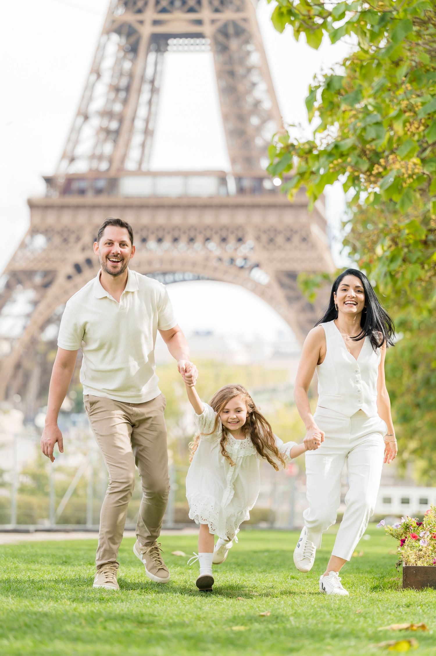 Family plays and runs together on grass with the iconic Eiffel Tower visible in background on sunny day in Paris.
