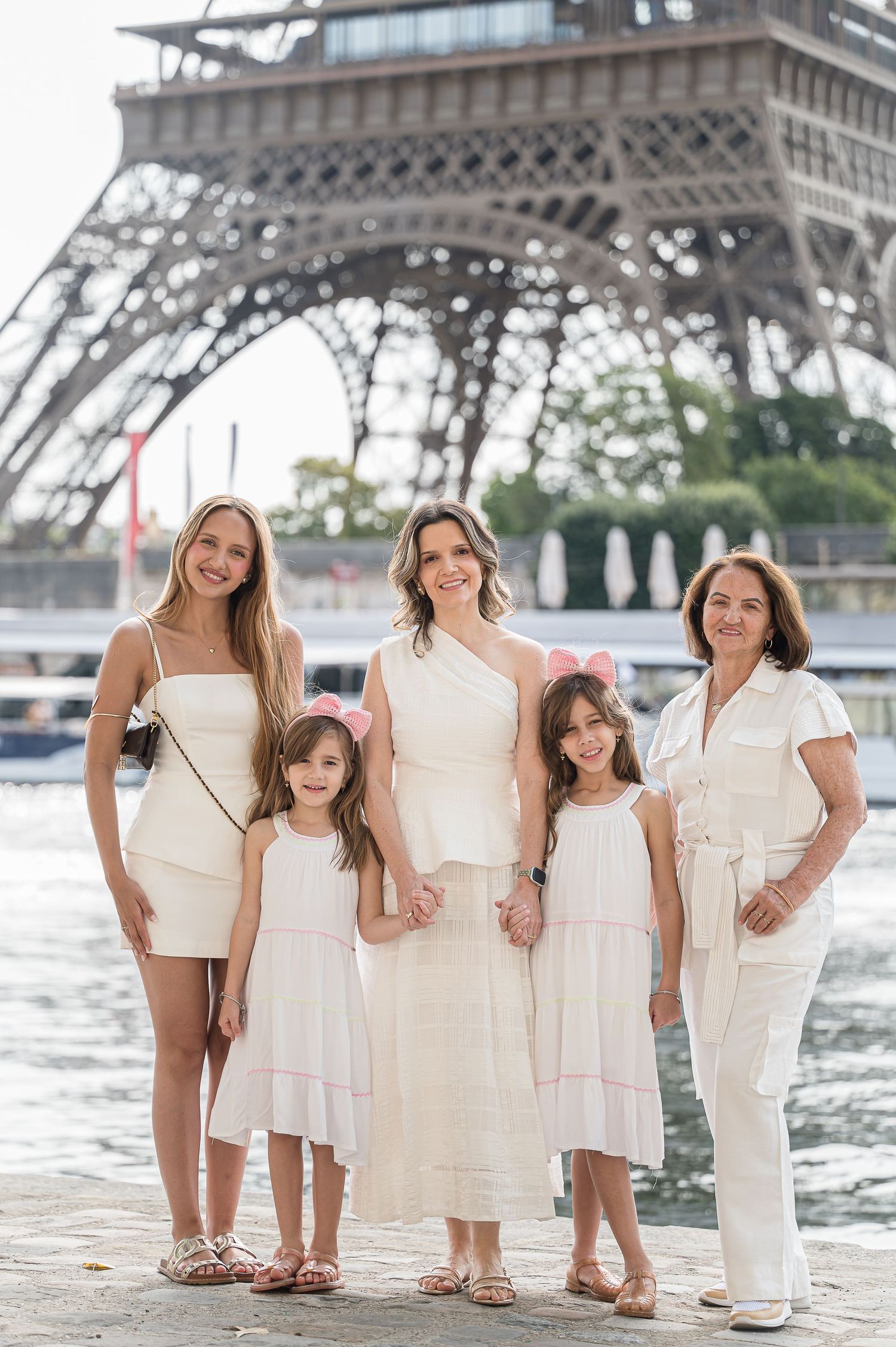 Five women in white outfits posing together in front of the Eiffel Tower in Paris, France.