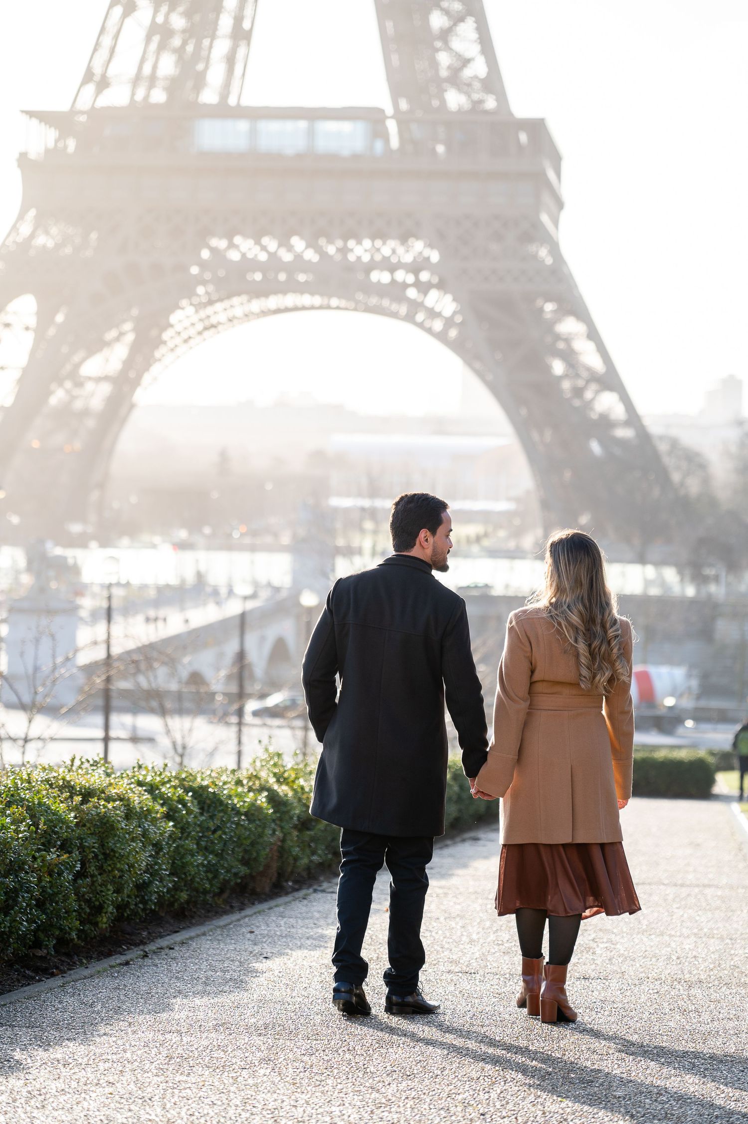A couple strolls along a path with the iconic Eiffel Tower framing their romantic moment.
