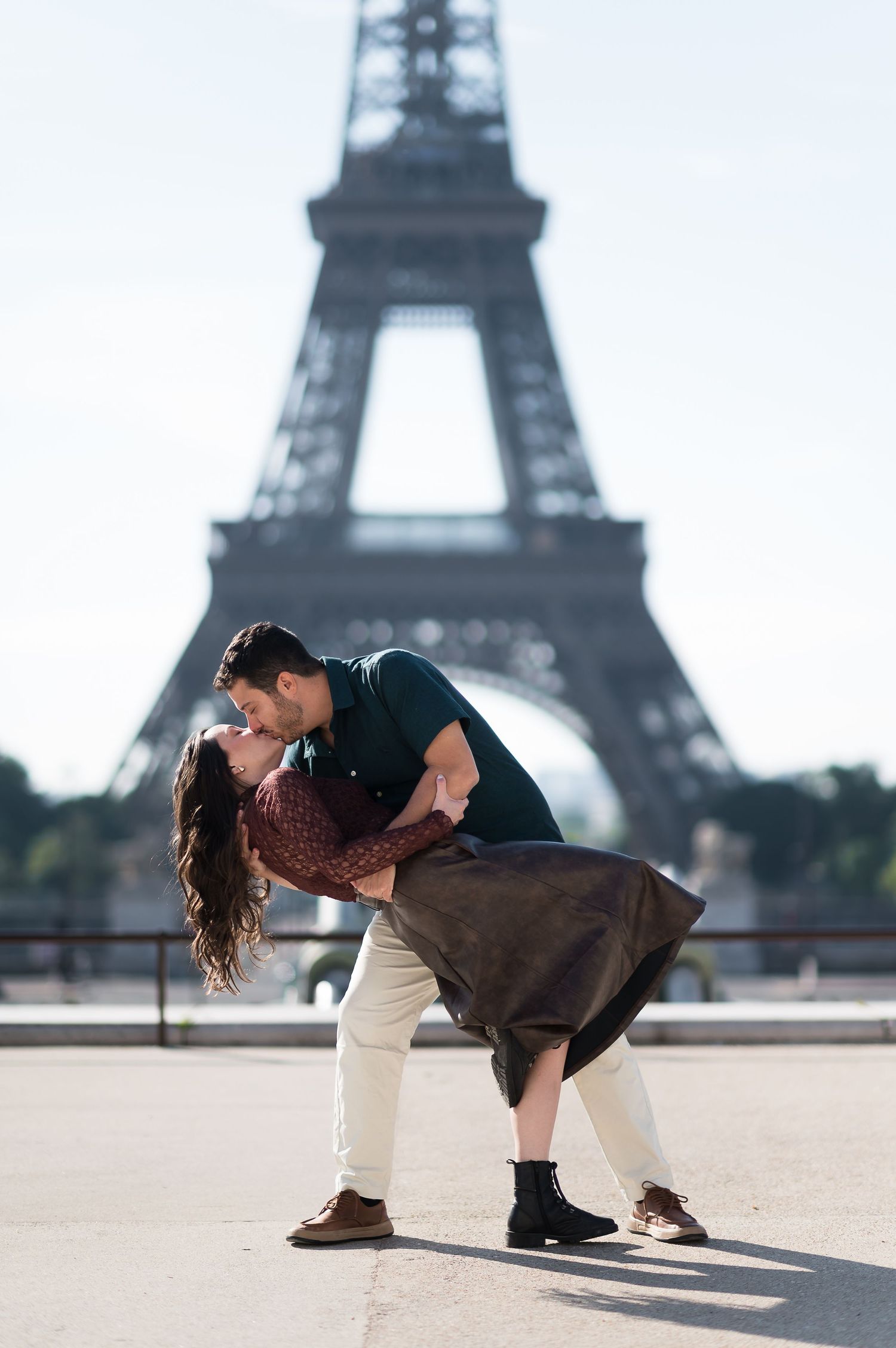 Romantic couple sharing a passionate dip kiss in front of the iconic Eiffel Tower in Paris, France.