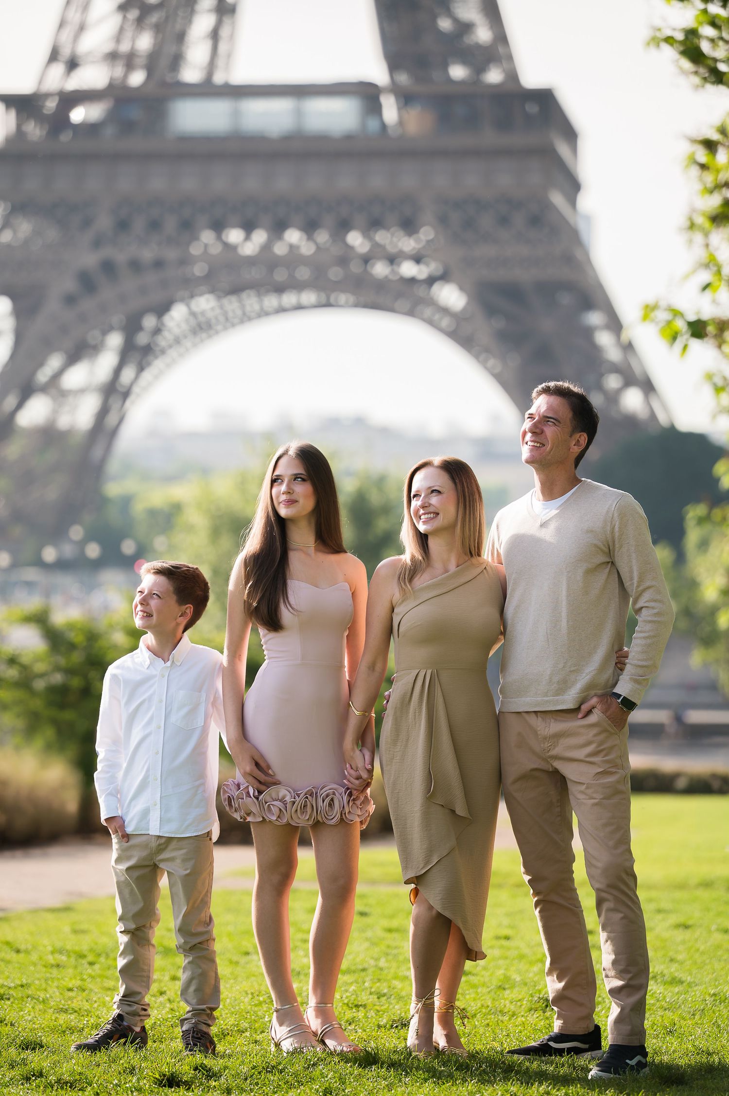 Family of four looking up joyfully with the Eiffel Tower rising behind them in Paris.