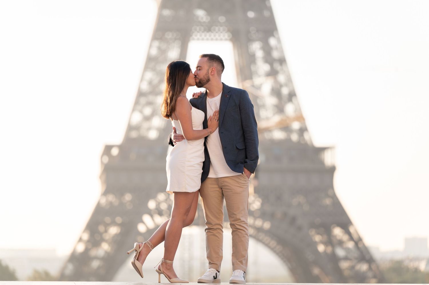 Romantic couple kissing in front of the Eiffel Tower in Paris, France on a sunny day.