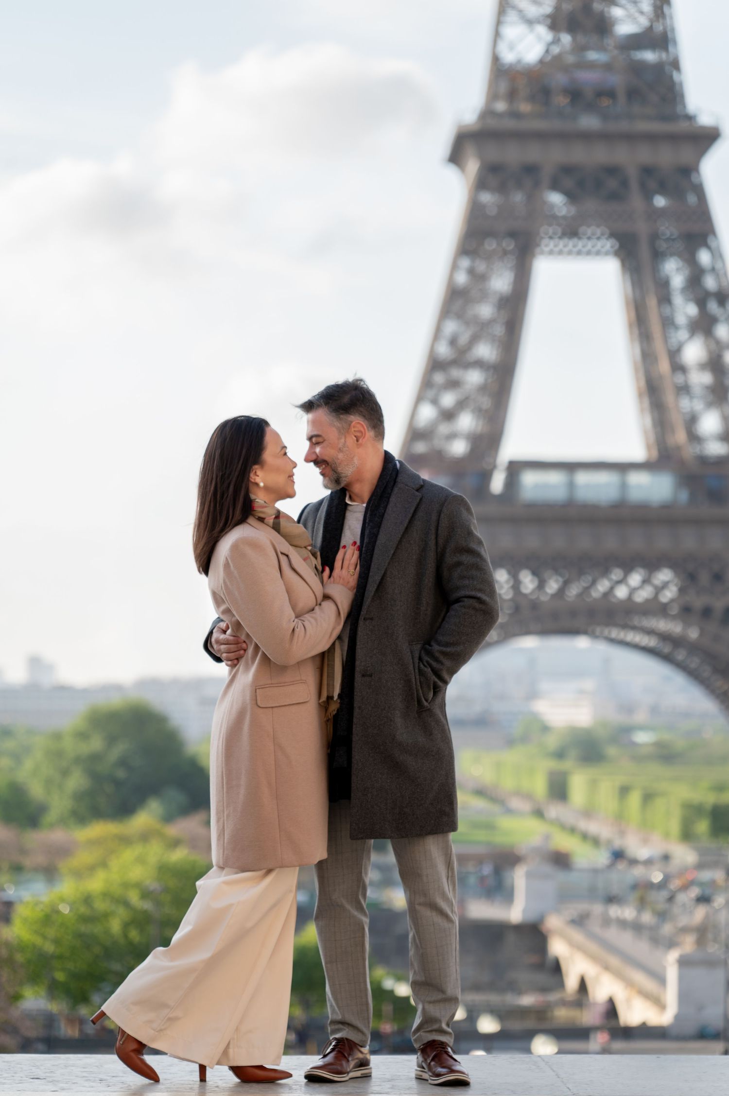 Romantic couple in stylish coats sharing a moment at Eiffel Tower viewpoint.