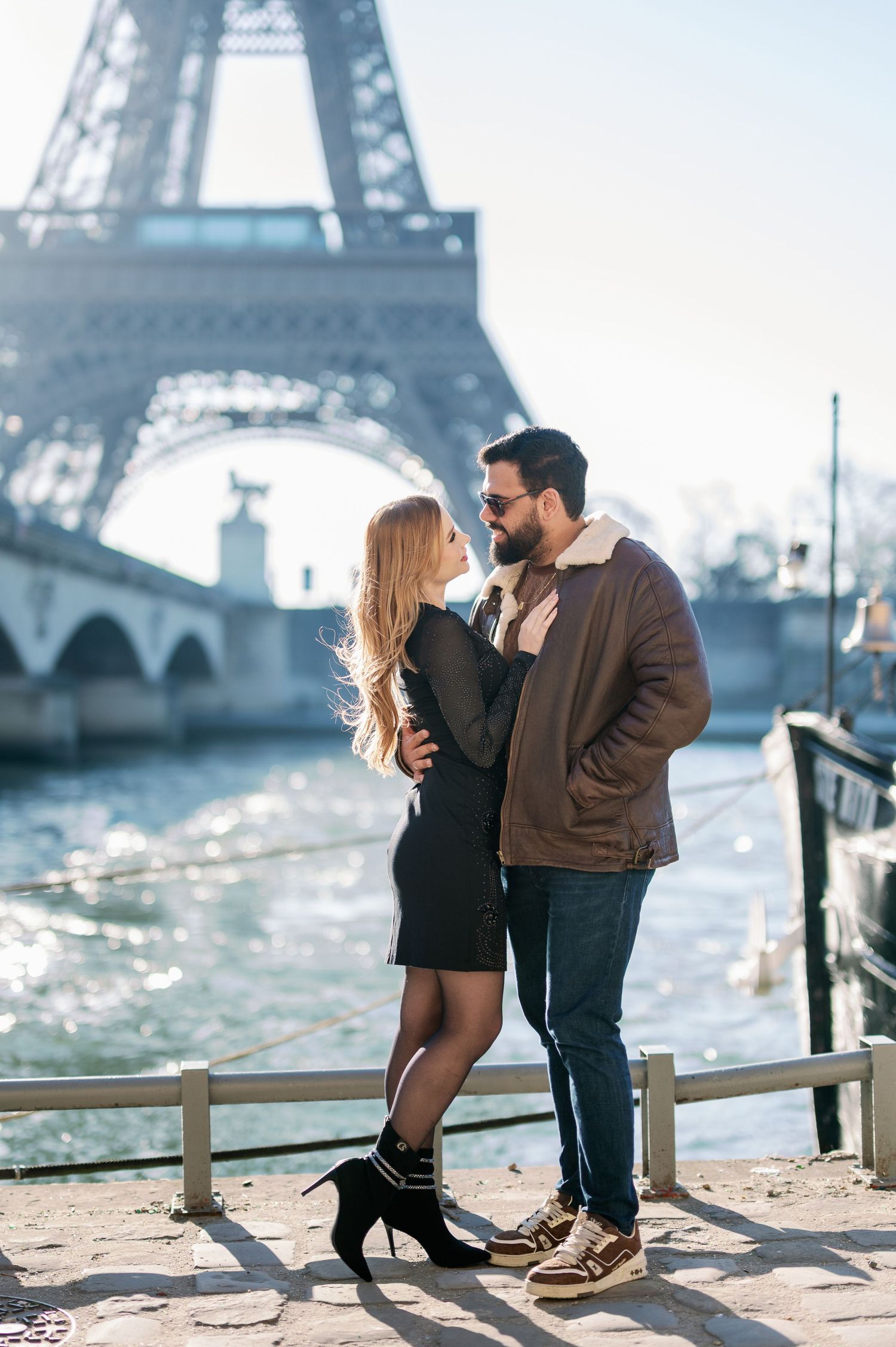 A romantic couple embraces by the Seine River with the Eiffel Tower as their backdrop in Paris.