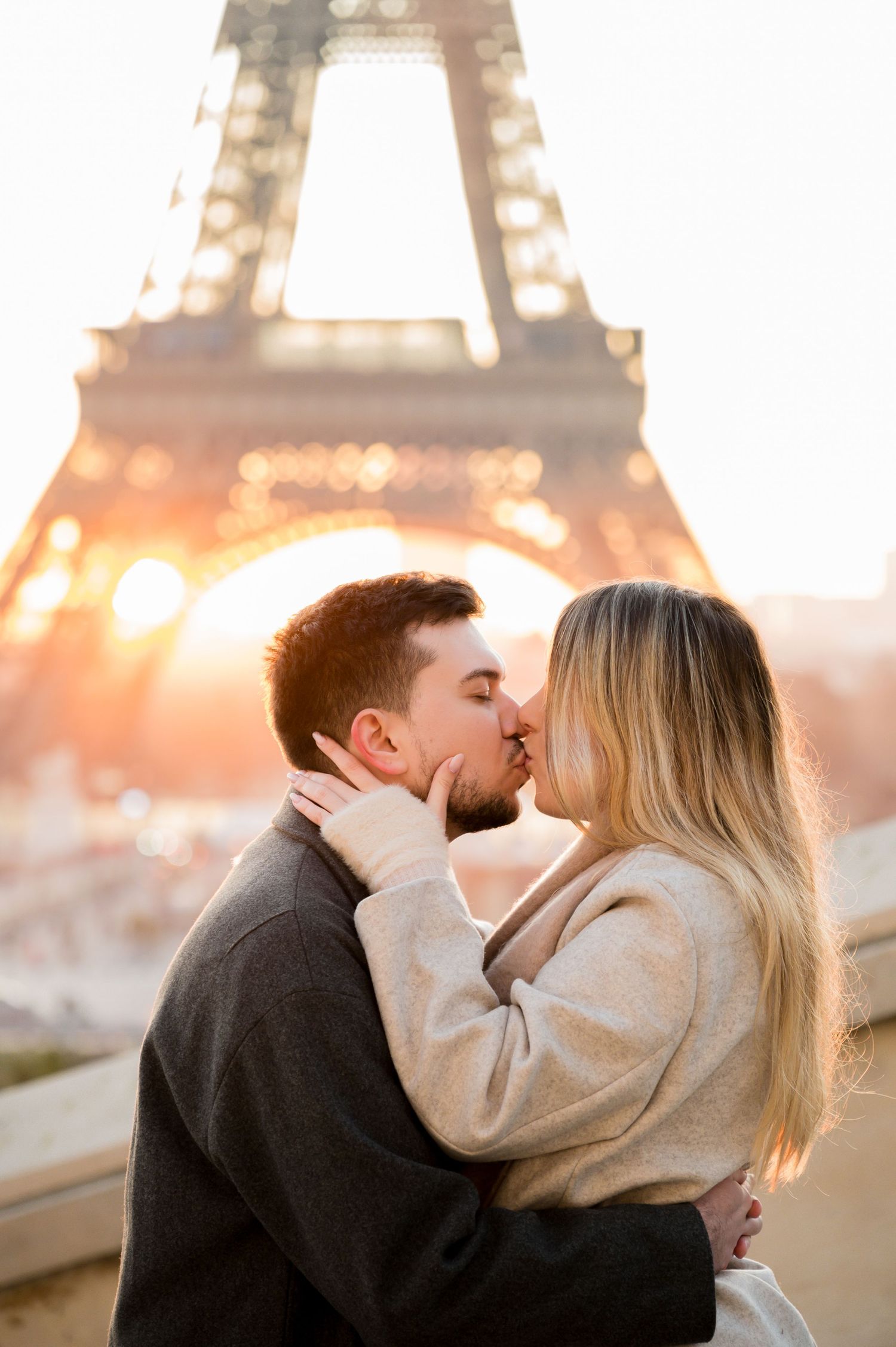 A romantic couple shares a tender kiss in front of the glowing Eiffel Tower at sunset in Paris.