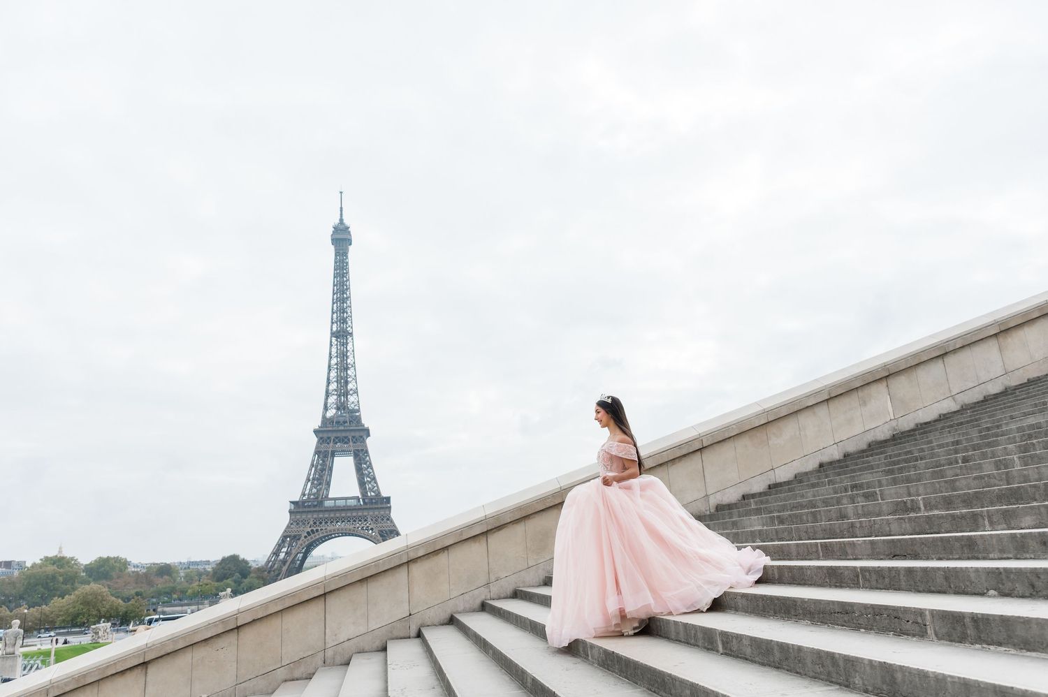 A person in a flowing pink dress poses gracefully on steps at Trocadero Square with the Eiffel Tower in Paris.