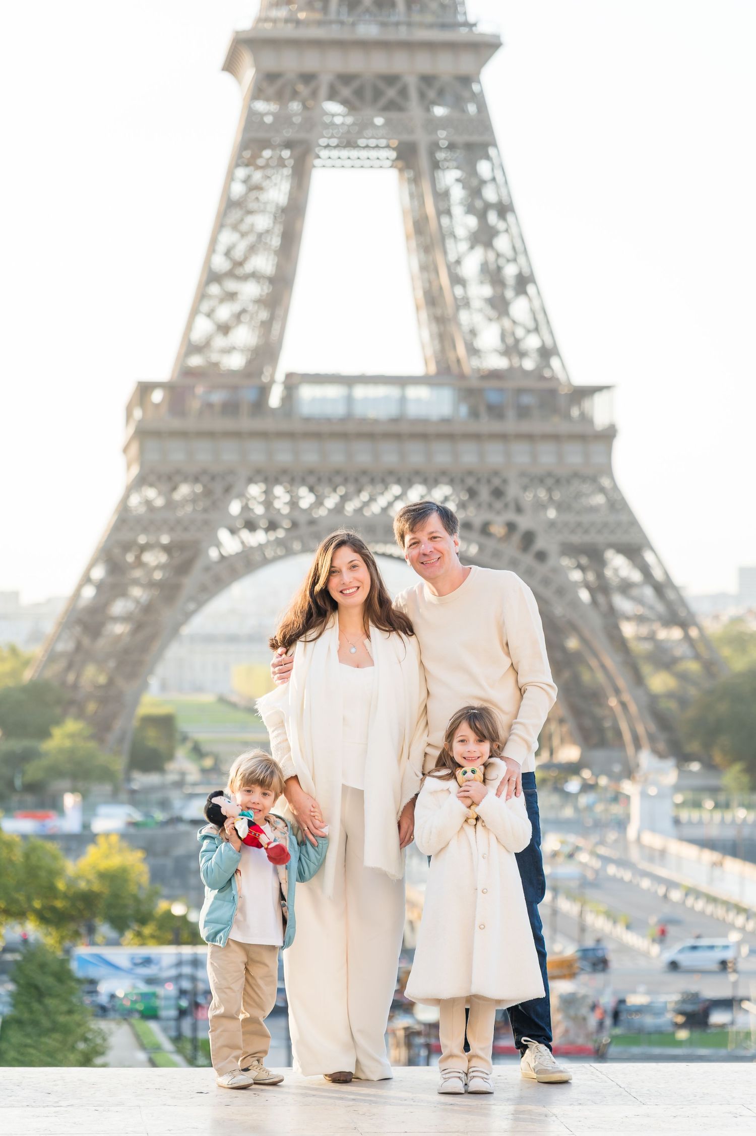 A family wearing white outfits poses together in front of the iconic Eiffel Tower in Paris.