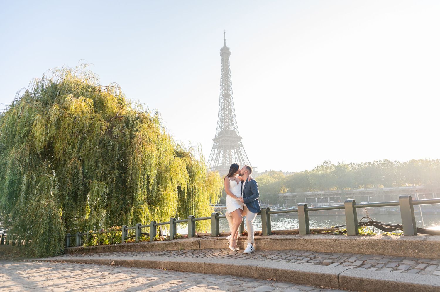 Romantic scene at sunset by the Seine River with the Eiffel Tower and weeping willows in the background.