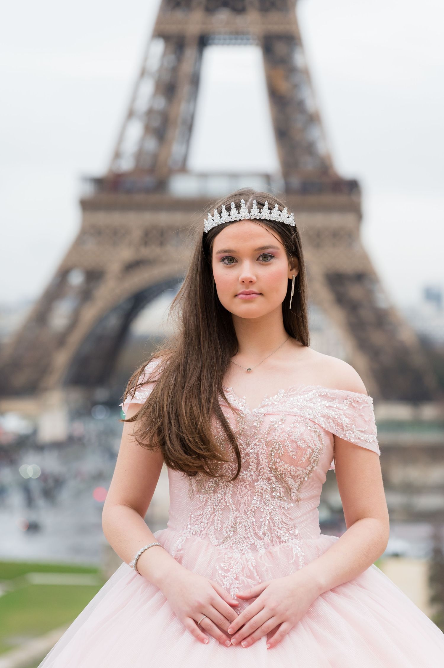 A person in a pink princess gown and tiara poses in front of the iconic Eiffel Tower in Paris.